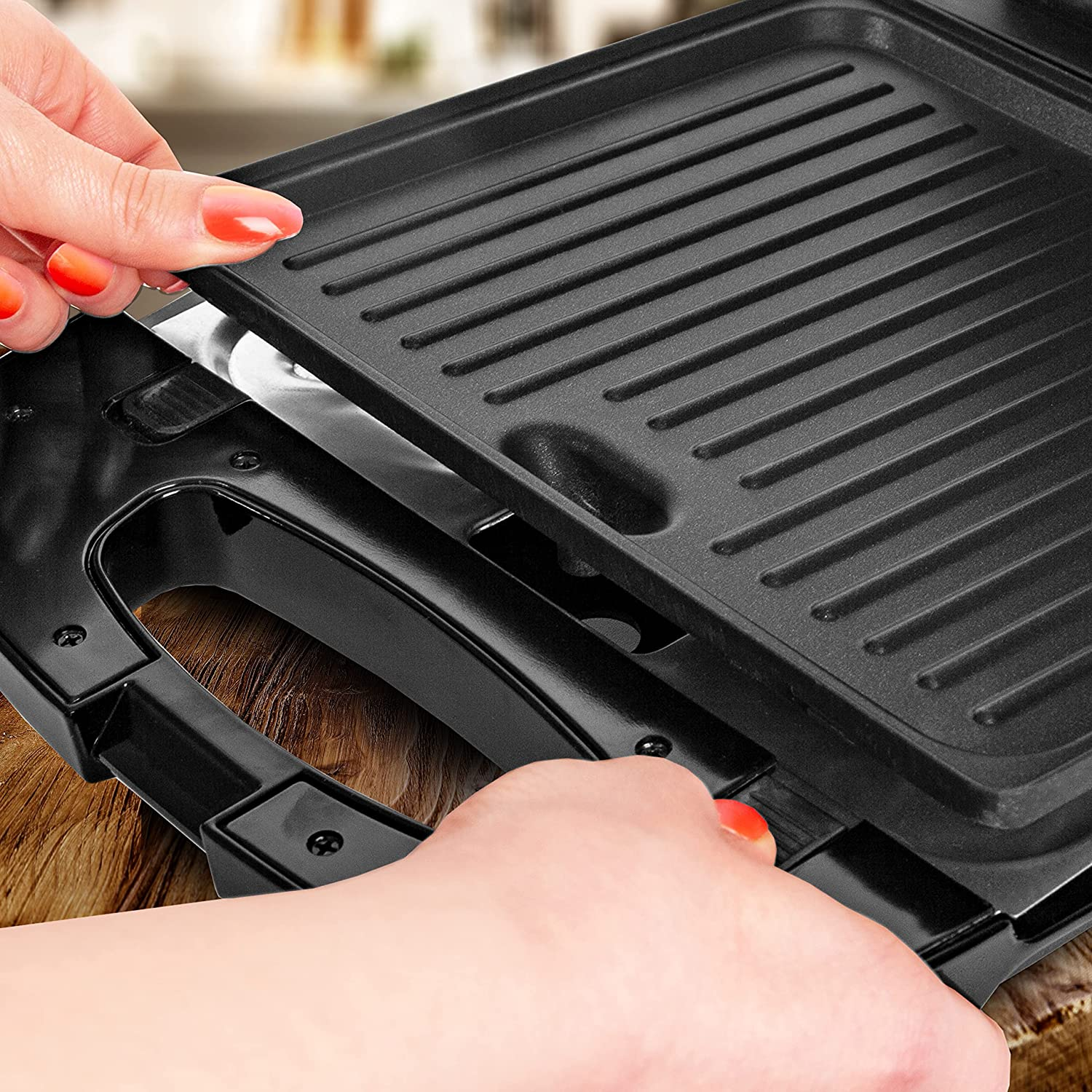 Hände, die eine Grillplatte von einem schwarzen Sandwichmaker entfernen und eine gerippte Heizfläche freilegen.