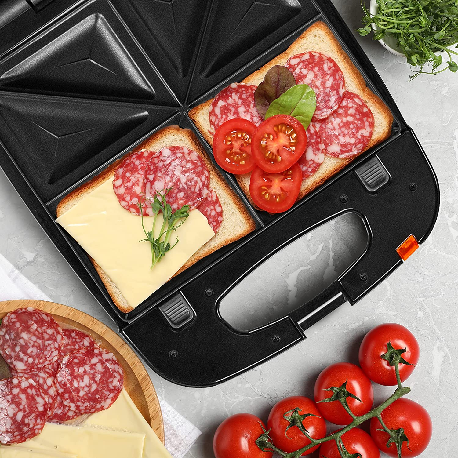 Ein Sandwichmaker mit zwei Sandwiches. Eines hat Käse und das andere Salami und Tomaten.