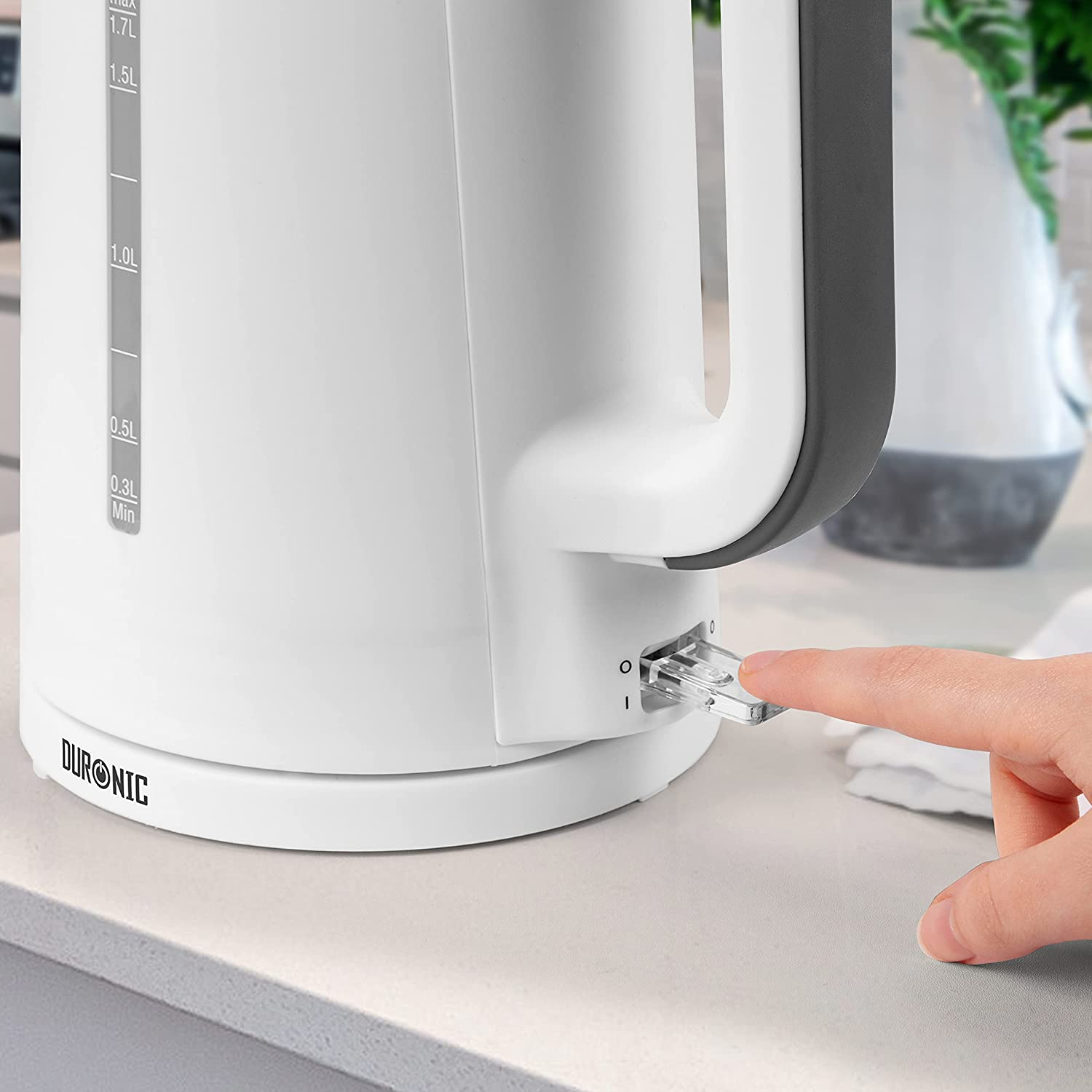 Ein weißer Wasserkocher mit einem Finger, der den Netzschalter drückt.