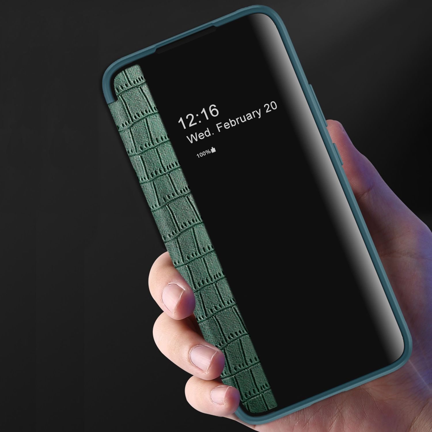 Hand, die ein Telefon mit einer grünen Krokodilmusterhülle hält. Der Bildschirm zeigt Datum und Uhrzeit auf schwarzem Hintergrund.