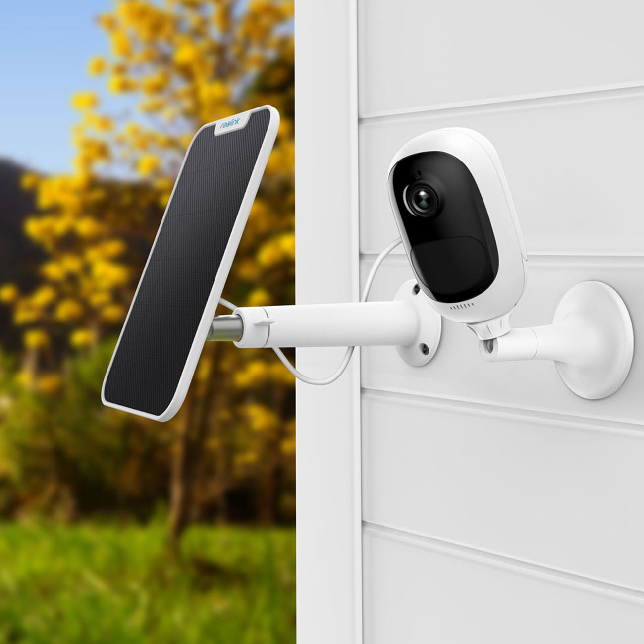 Weiße und schwarze Überwachungskamera und Solarpanel an einer weißen Wand montiert. Der Hintergrund ist ein grüner Garten.