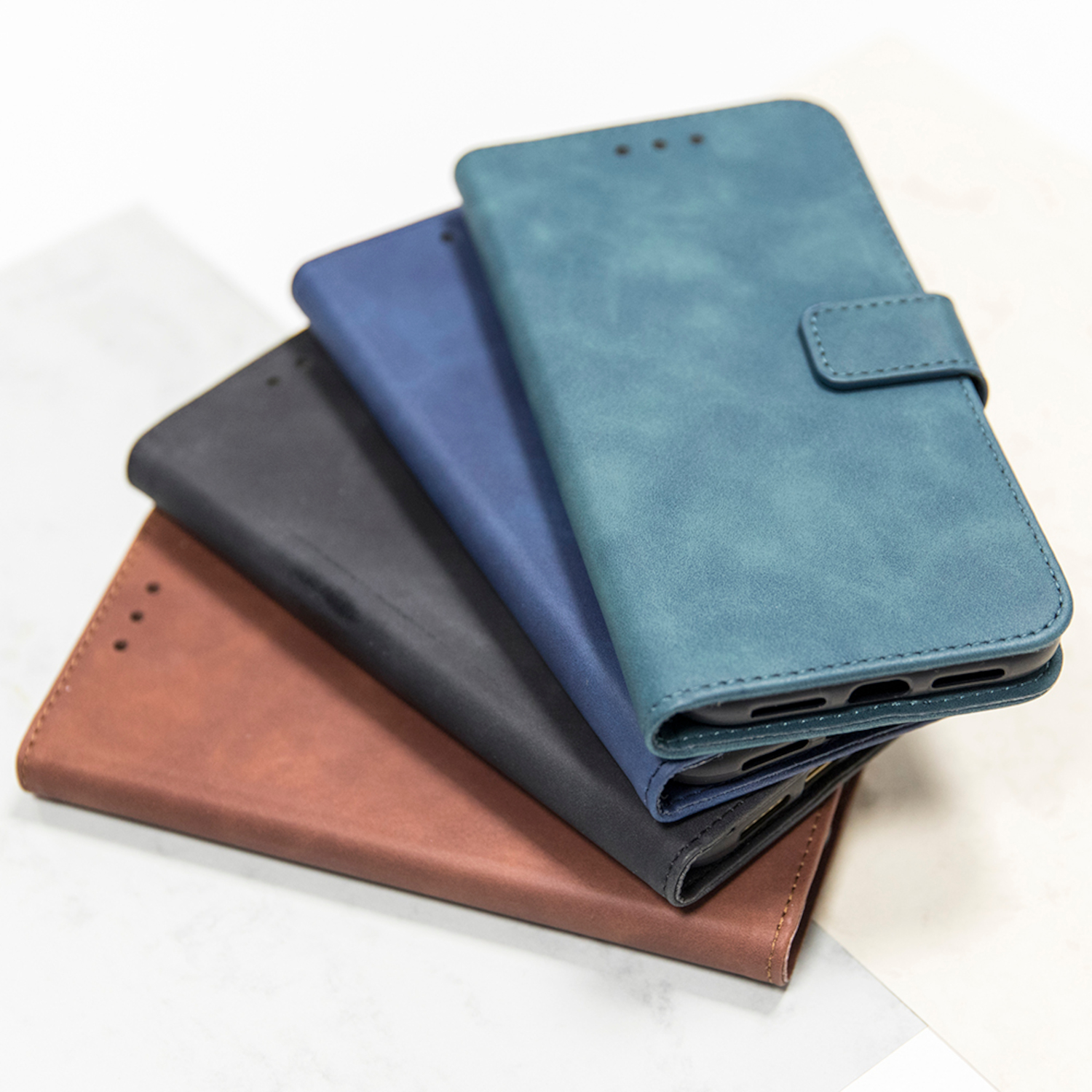 Ein Stapel von vier Handyhüllen in verschiedenen Farben: Braun, Schwarz, Blau und Türkis.