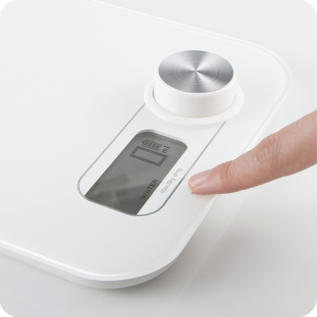 Biała cyfrowa waga kuchenna. Palec naciska przycisk na powierzchni wagi.