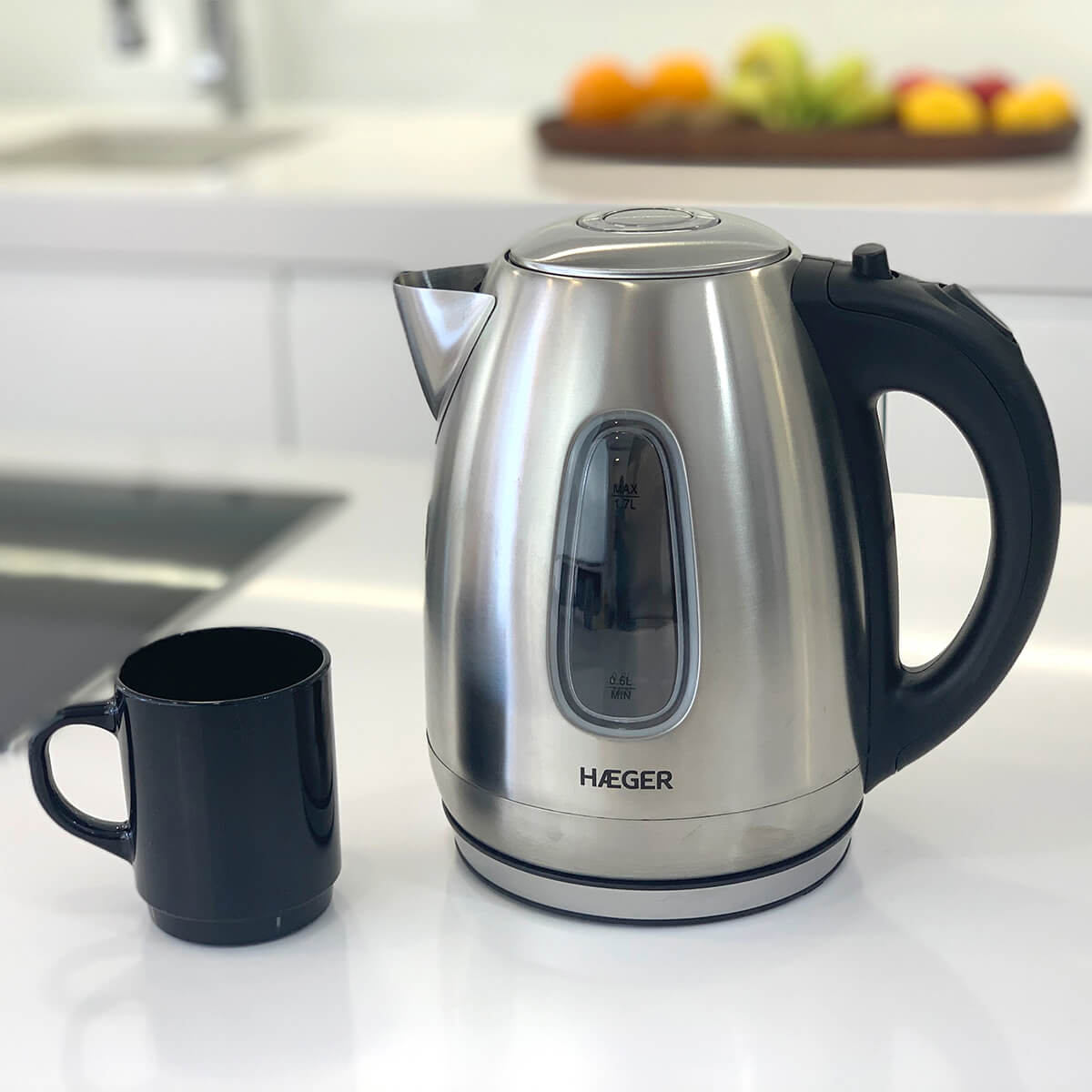 Bollitore elettrico in acciaio inox, tazza nera su piano bianco. Sfondo cucina.