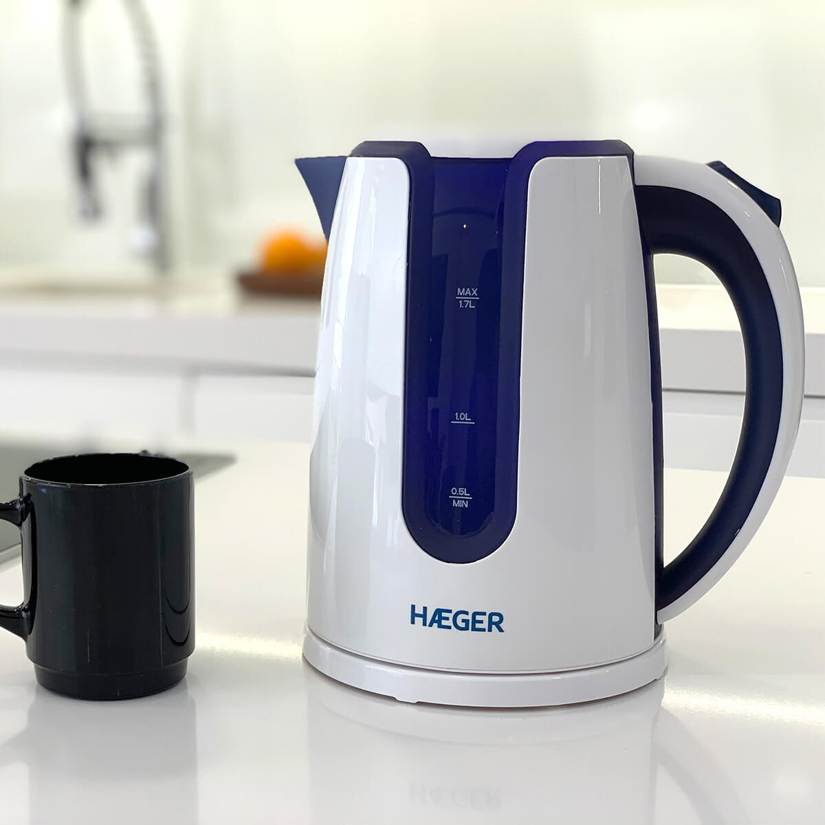 Hervidor eléctrico blanco y azul sobre una superficie blanca. Una taza negra está cerca.