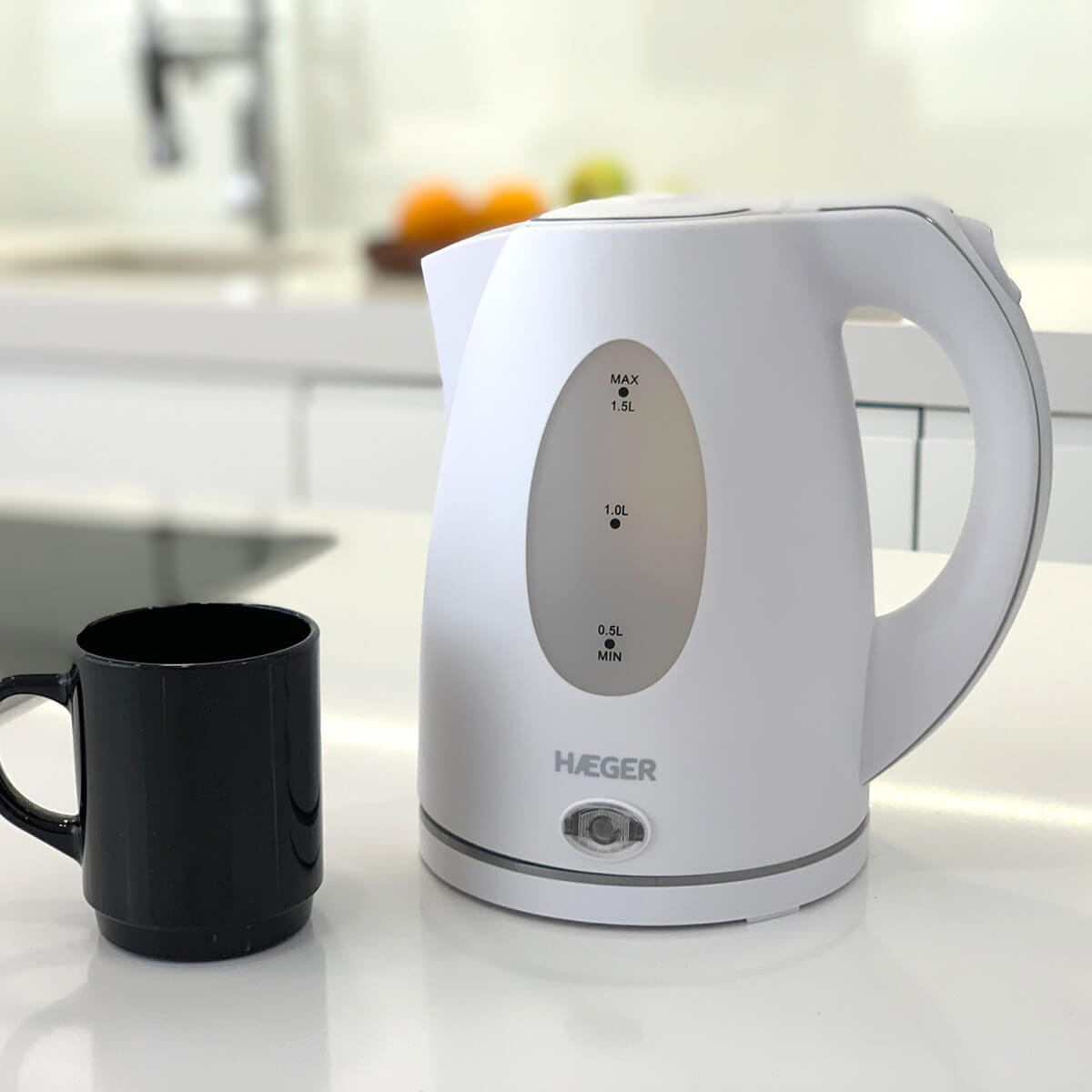 Un bollitore elettrico bianco con una tazza nera su un bancone. Una cucina è visibile sullo sfondo.