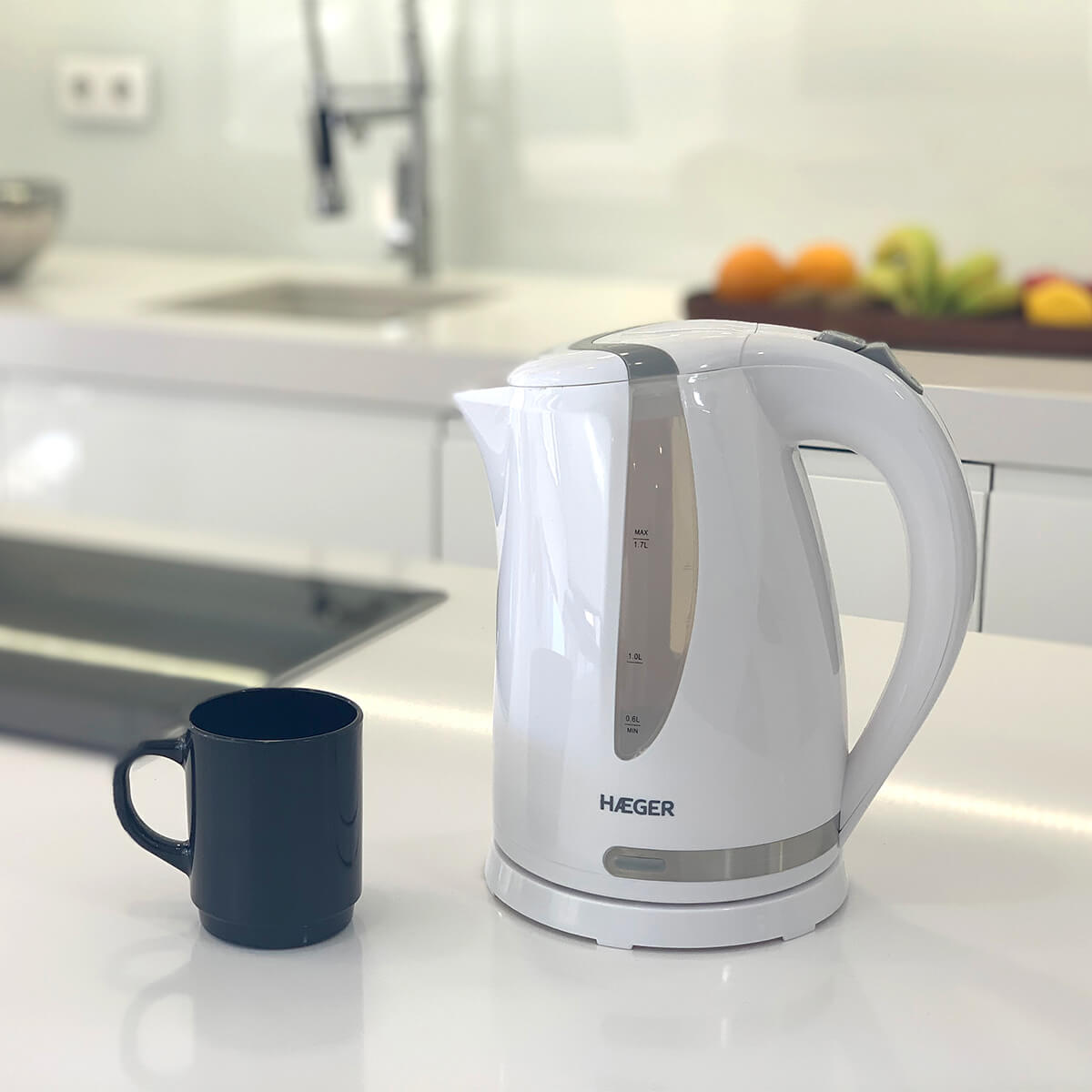 Hervidor eléctrico blanco y taza negra sobre encimera blanca. Fondo de cocina.