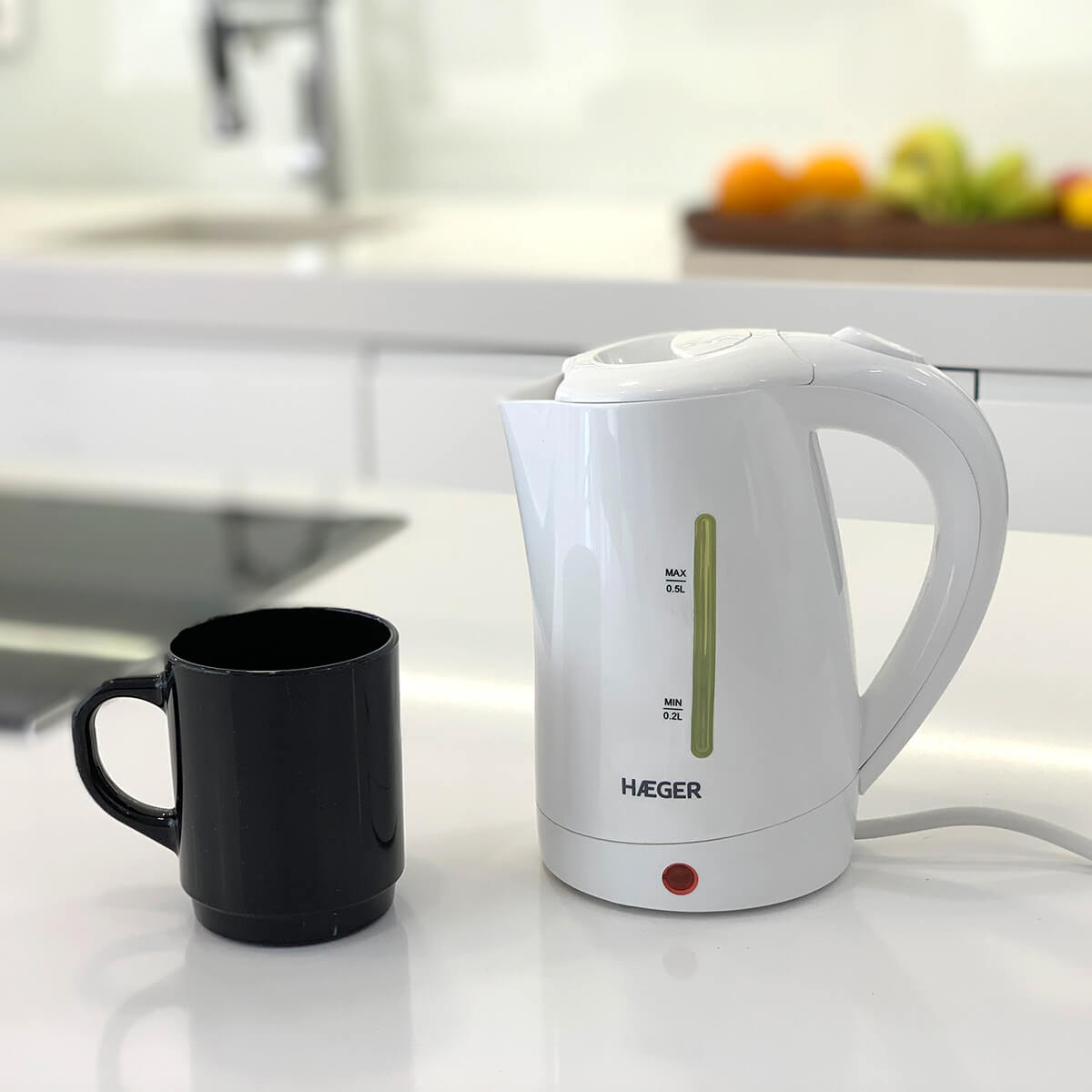Un bollitore elettrico bianco con una tazza nera su una superficie bianca.