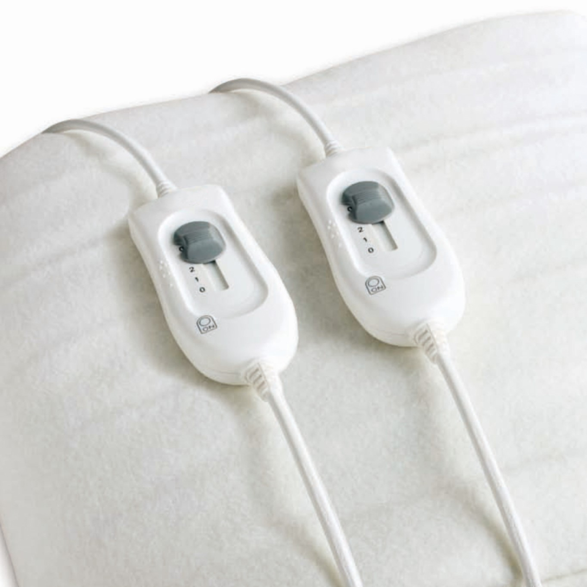 Twee witte elektrische verwarmingskussencontrollers met grijze draaiknoppen op een wit verwarmingskussen.