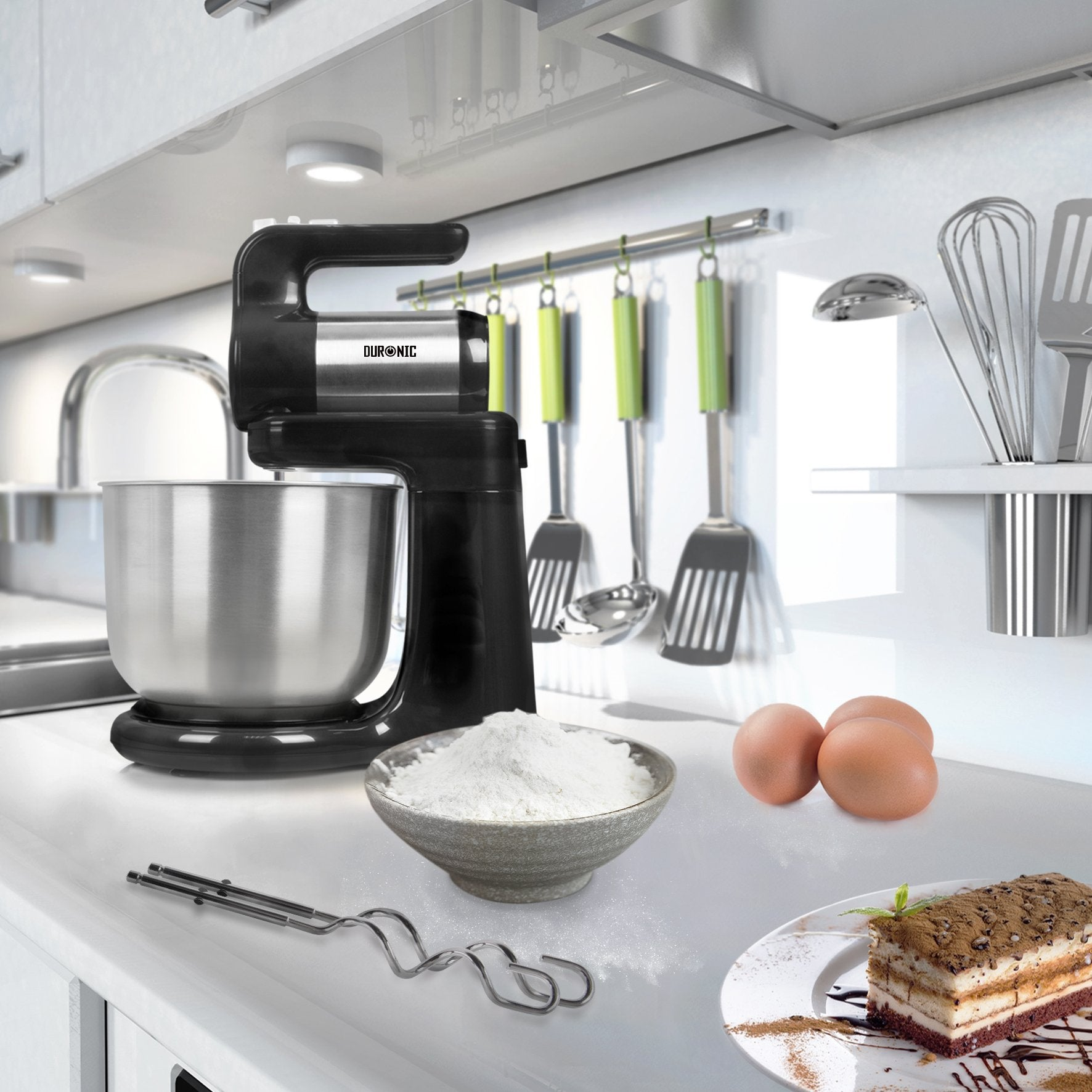 Schwarzer Küchenmixer mit Schüssel und Zutaten auf weißer Theke. Küchenutensilien im Hintergrund.