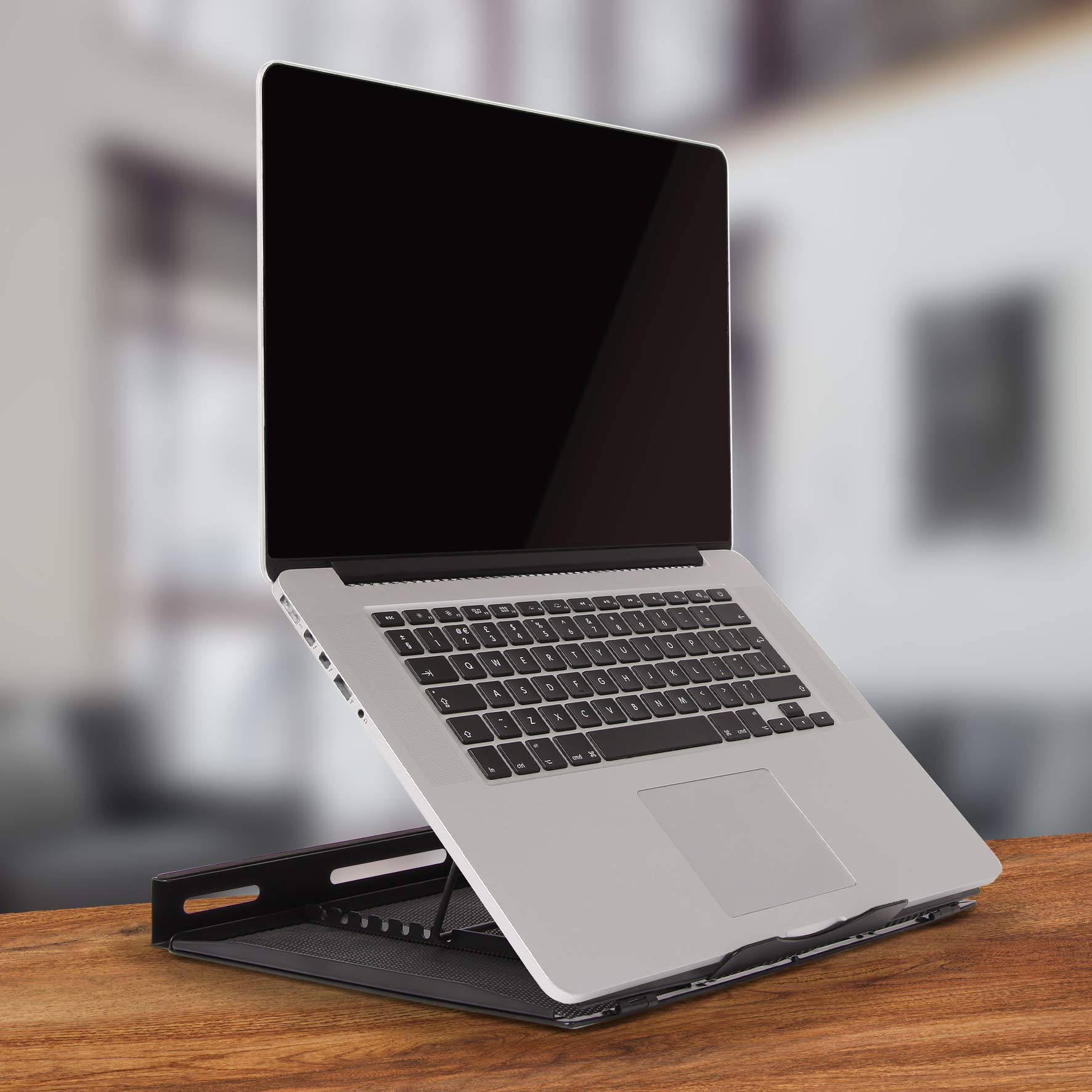Laptop en un soporte elevado, colocado sobre una mesa de madera. Fondo borroso.