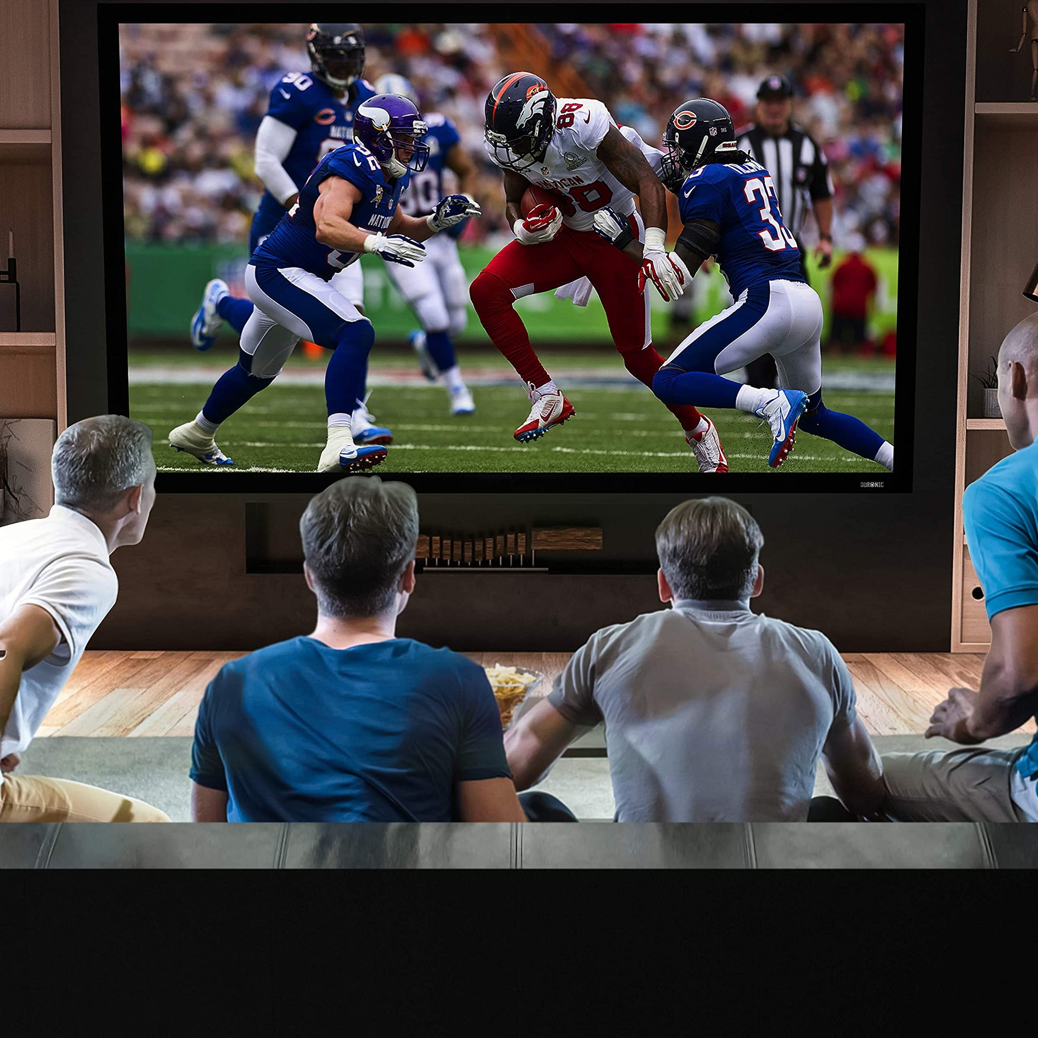 Grupo de personas viendo un partido de fútbol en un televisor de pantalla grande en una habitación.