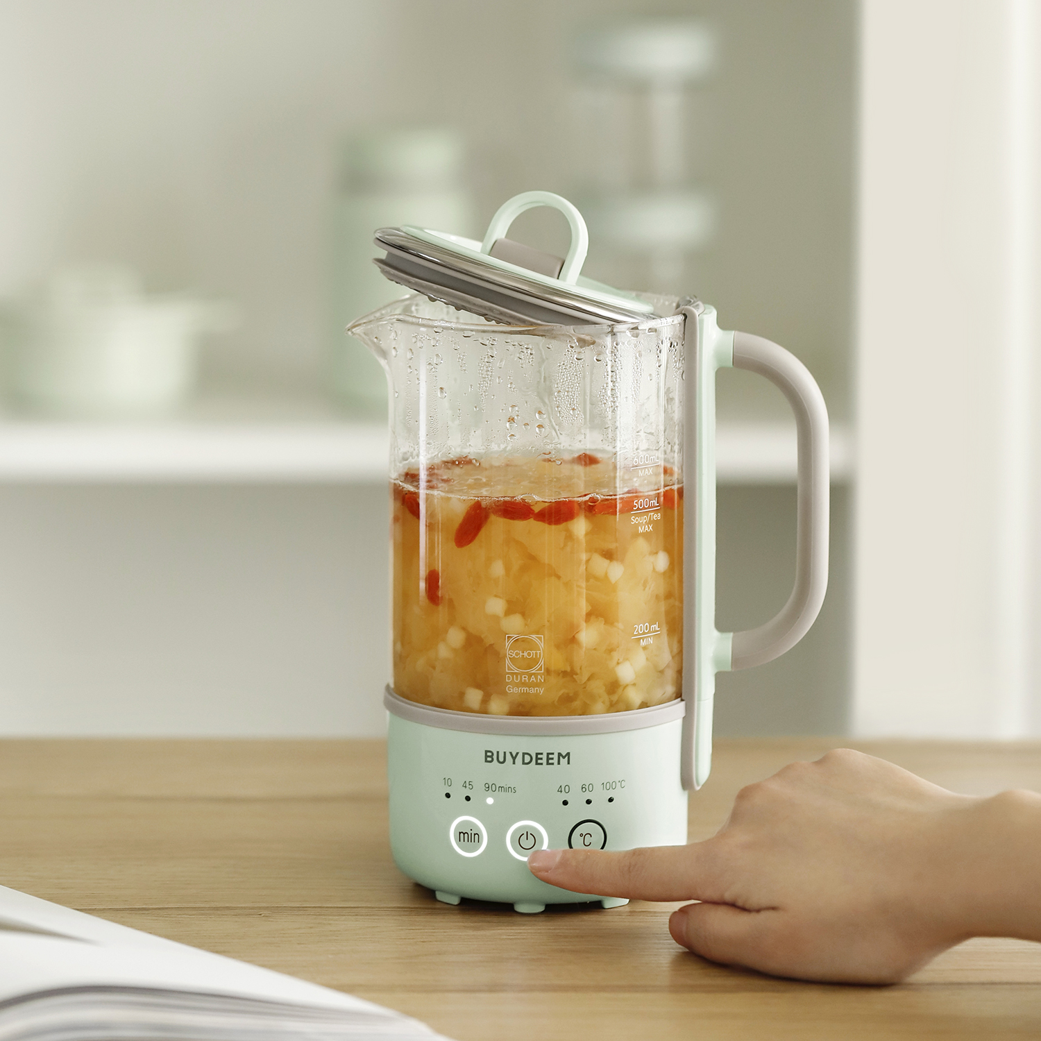 Palec osoby naciska przycisk na małym szklanym urządzeniu. Ma uchwyt i zieloną podstawę.