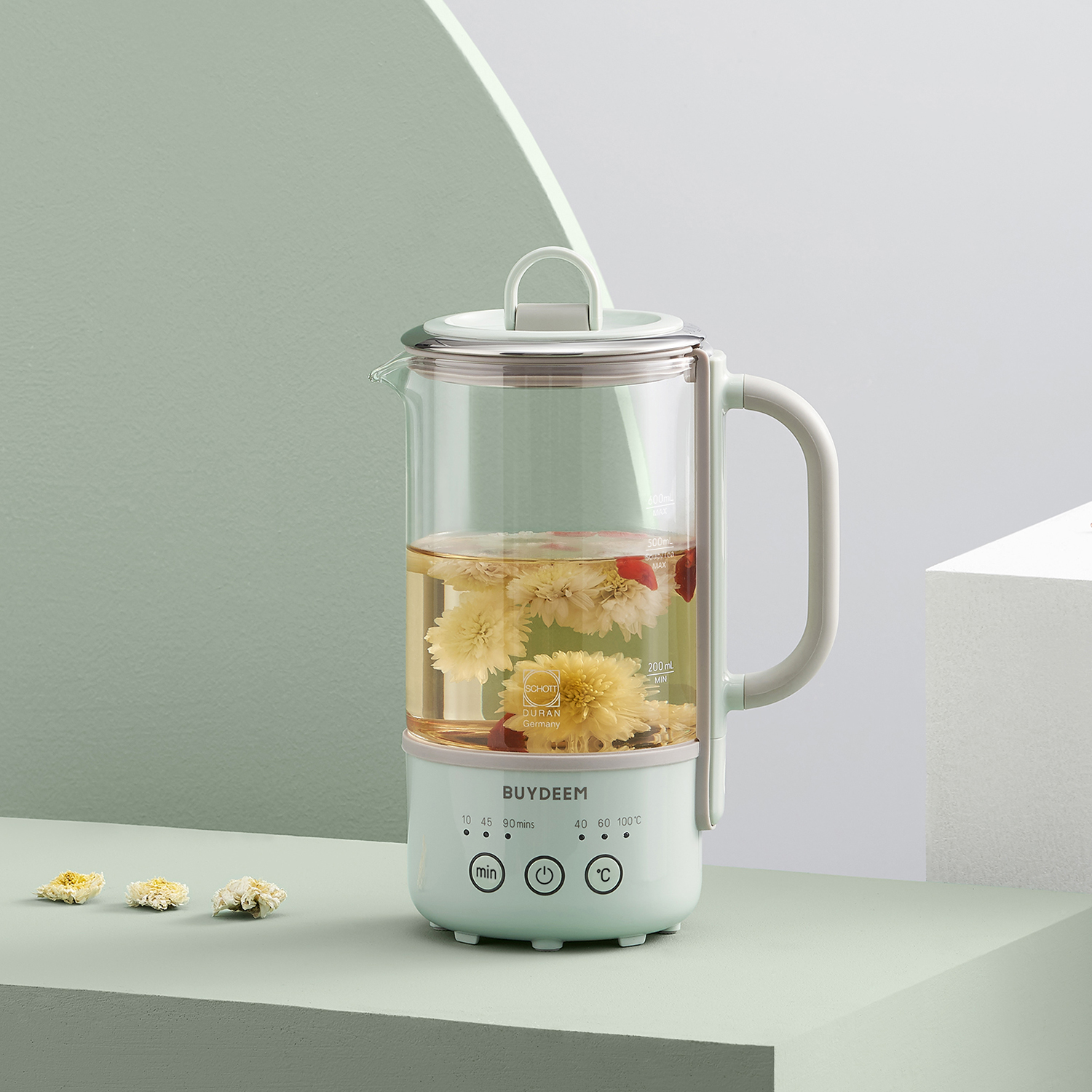 Szklany dzbanek do herbaty z kwiatami na zielono-białej powierzchni, biały uchwyt.