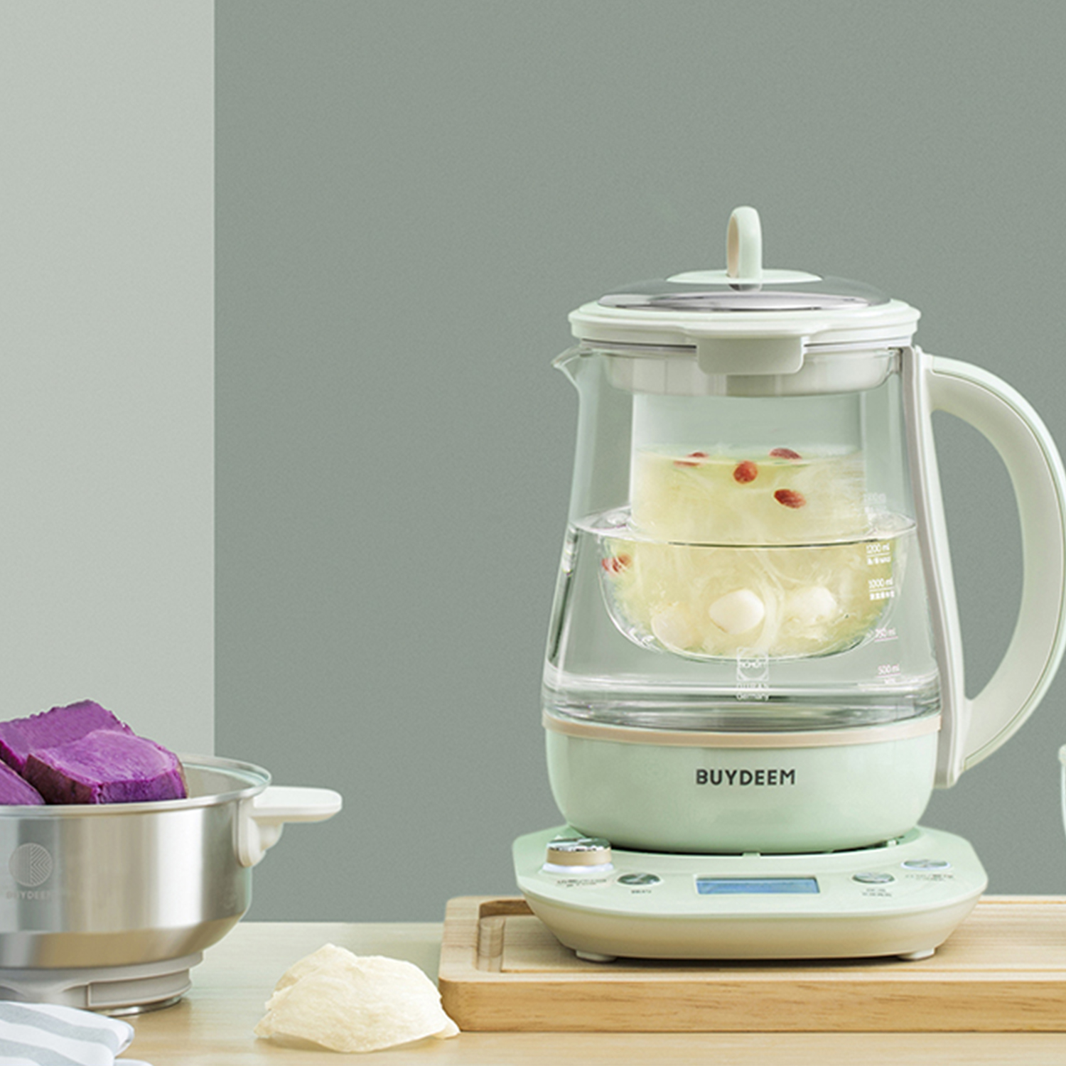 Szklany ekspres do herbaty z jasnozieloną podstawą, zawierający herbatę i składniki, z drewnianą tacą.