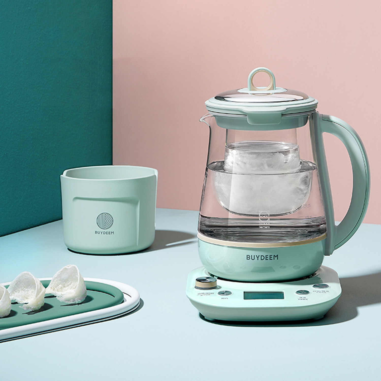 Scena w kolorze turkusowym i różowym ze szklanym czajnikiem na podstawie, miską i tacą z jedzeniem.