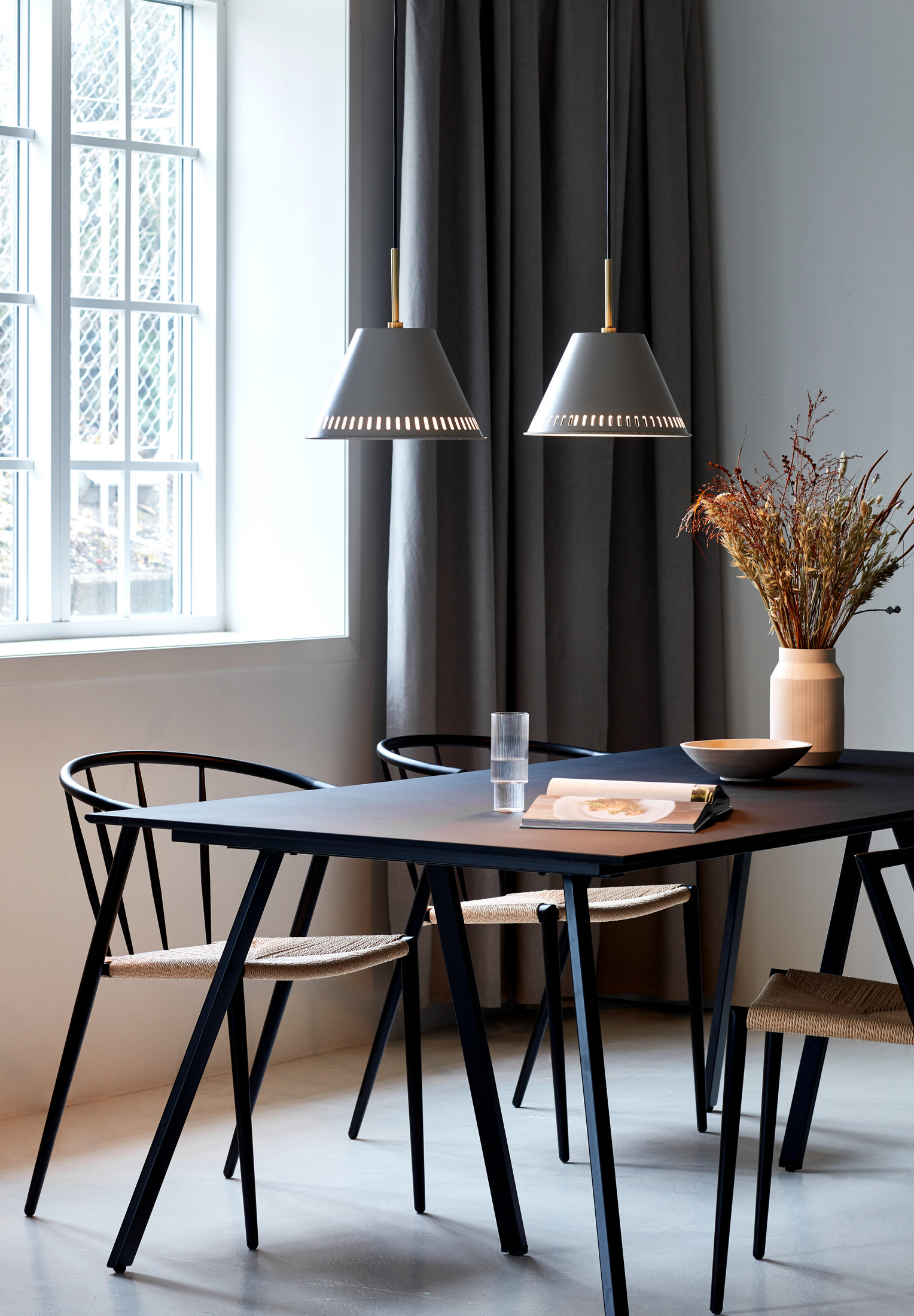 Esszimmer: zwei hängende graue Lampen, Tisch mit Stühlen, Fenster, Vorhang und Vase.