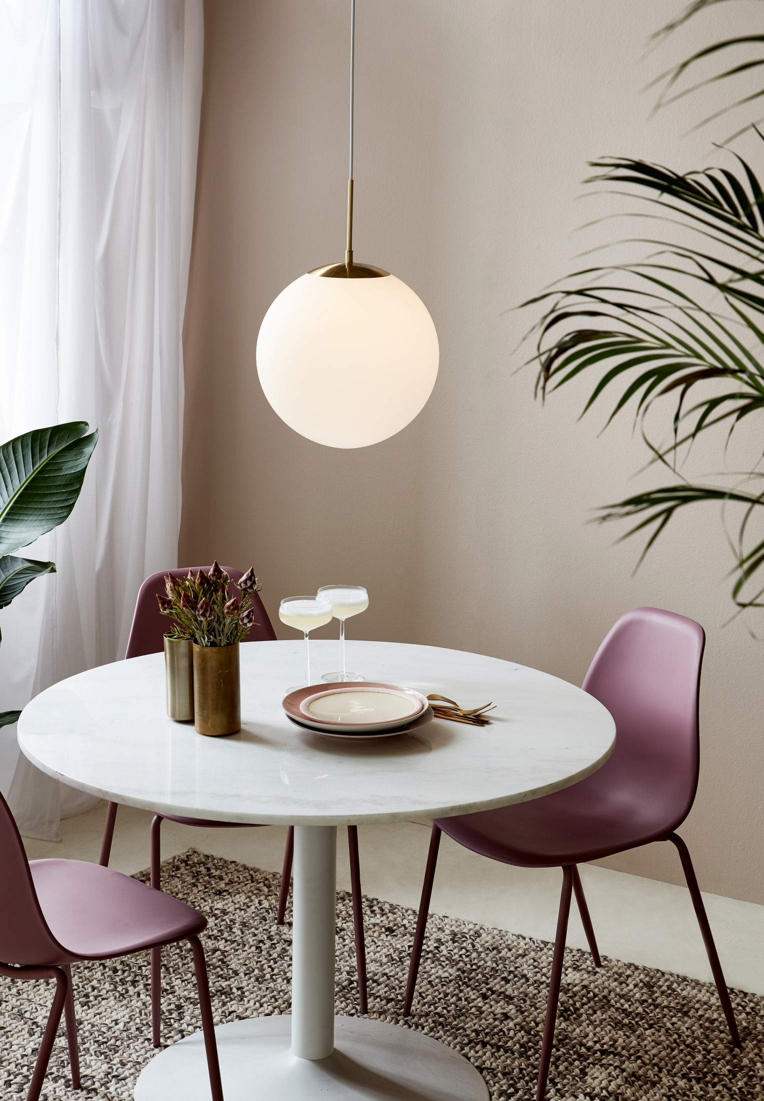 Une suspension globe blanche. Elle est suspendue au-dessus d'une table blanche avec deux verres et une assiette.