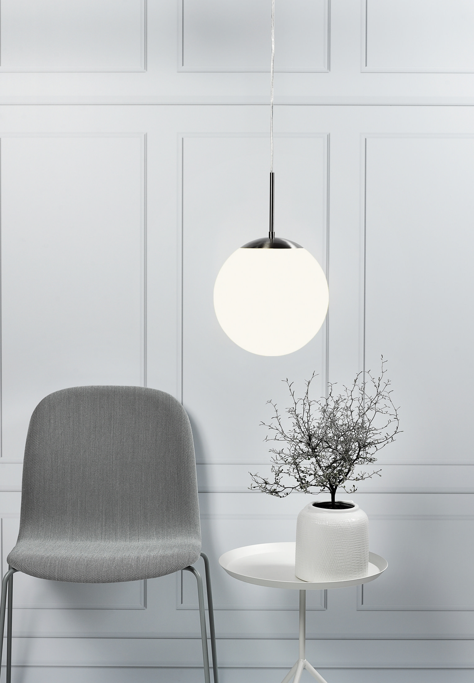 Une lampe sphérique blanche suspendue au-dessus d'une table avec une plante et une chaise grise.
