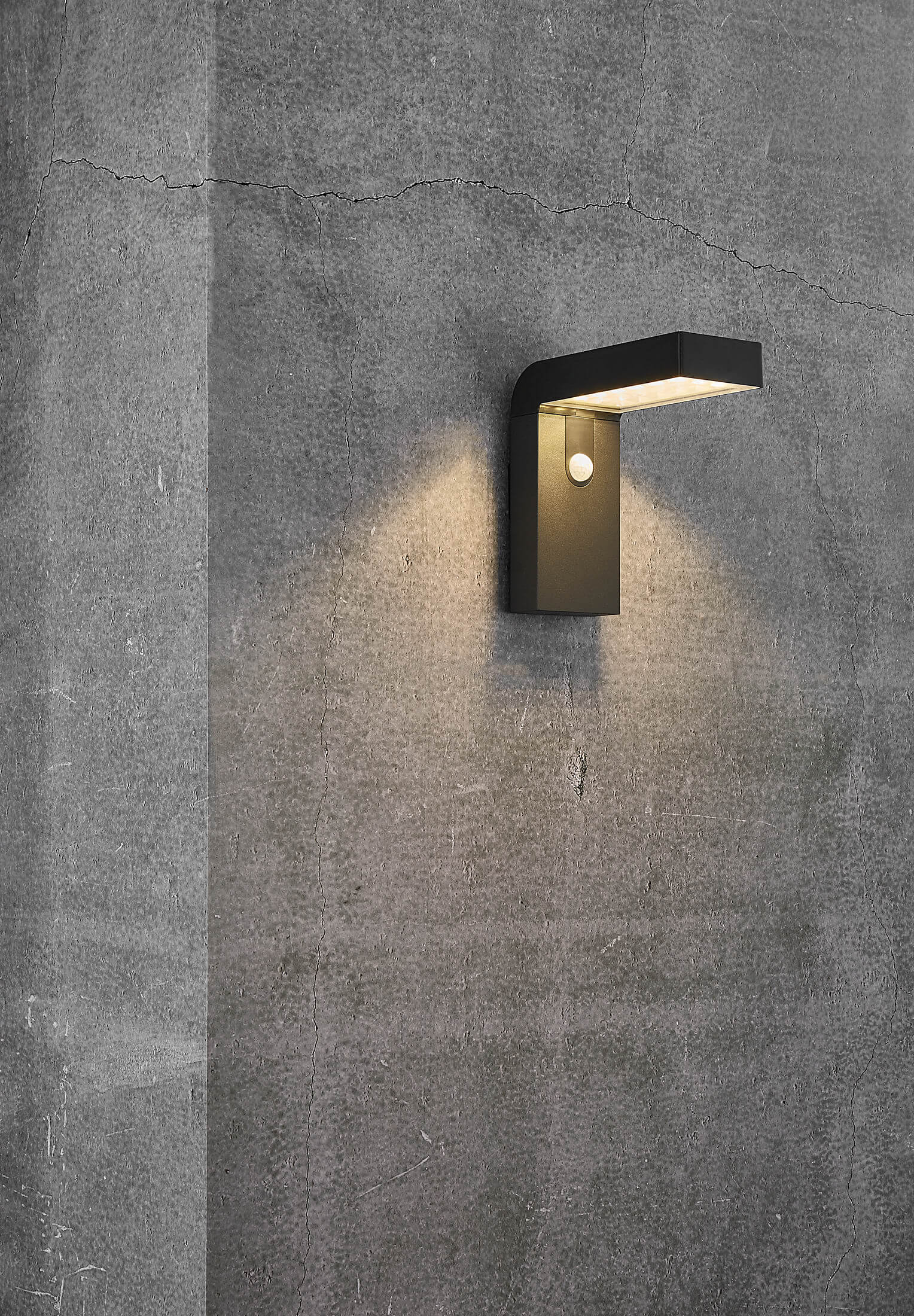 Schwarze Außenwandleuchte an einer Betonwand, mit einzelner Lichtemission.