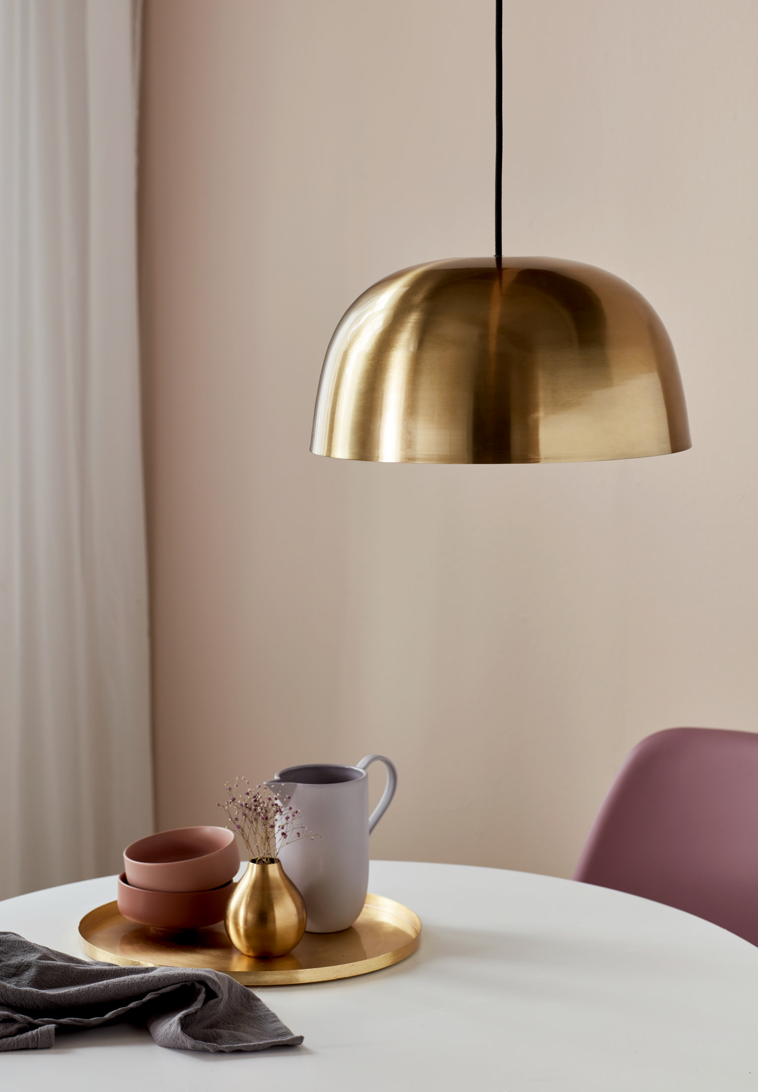 Eine goldene Pendelleuchte hängt über einem Tisch mit Schalen und einer Vase.