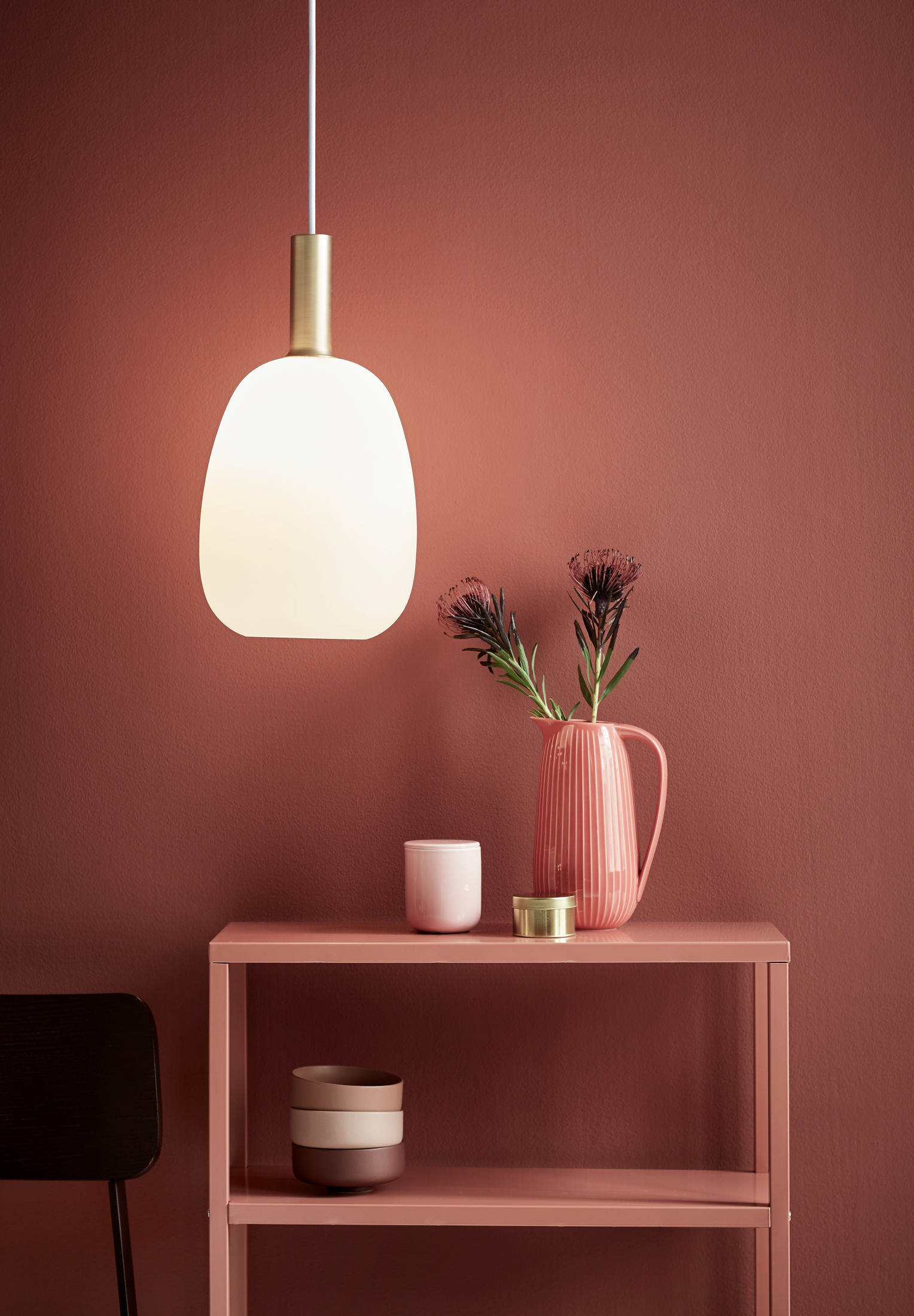 Une lampe suspendue au-dessus d'une table rose avec des fleurs, une tasse et un récipient décoratif.