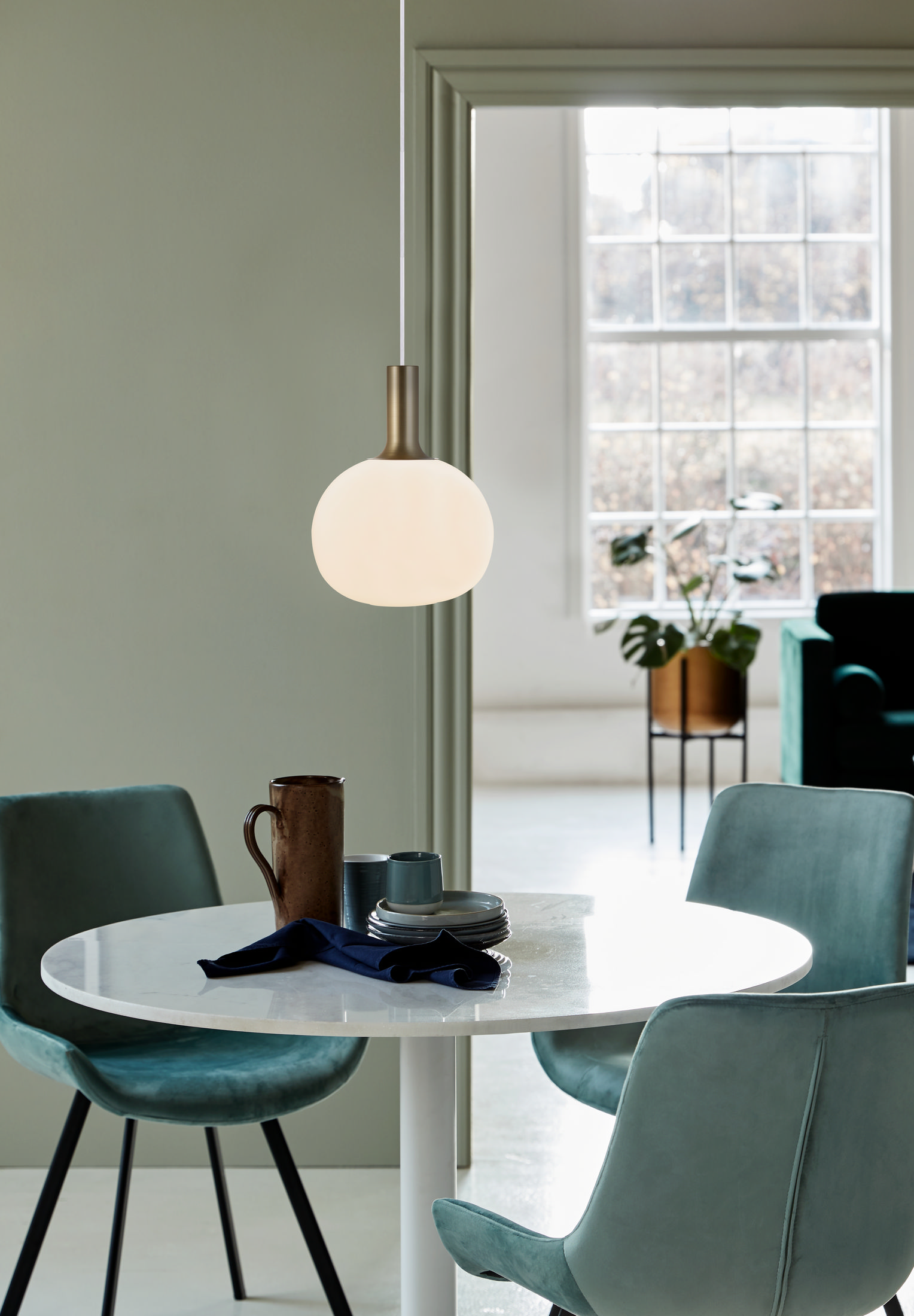 Une table ronde blanche avec un luminaire au-dessus. Chaises et décor bleu-vert en arrière-plan.