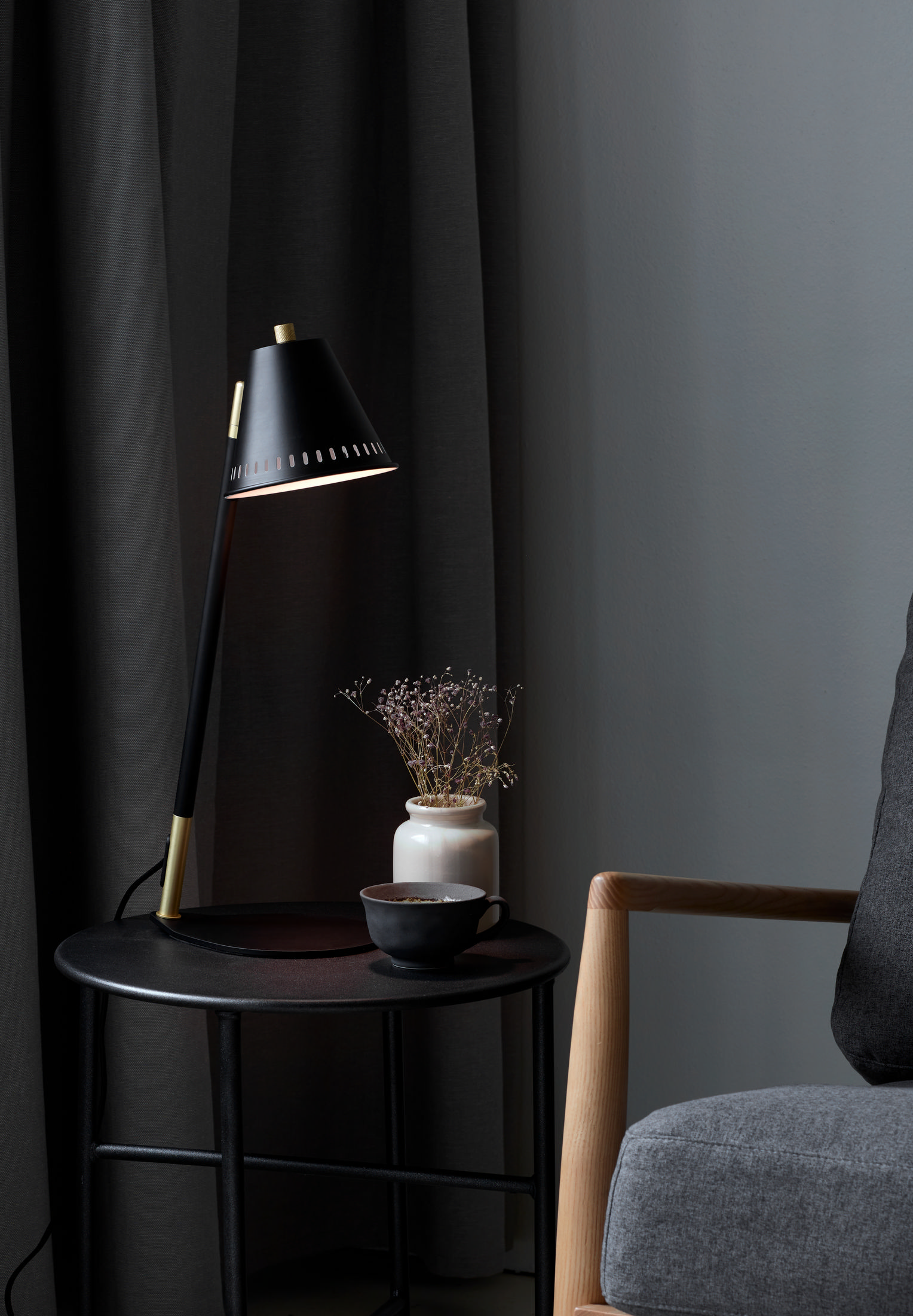 Schwarze Schreibtischlampe auf rundem Tisch mit Vase und Tasse. Dunkelgrauer Hintergrund.