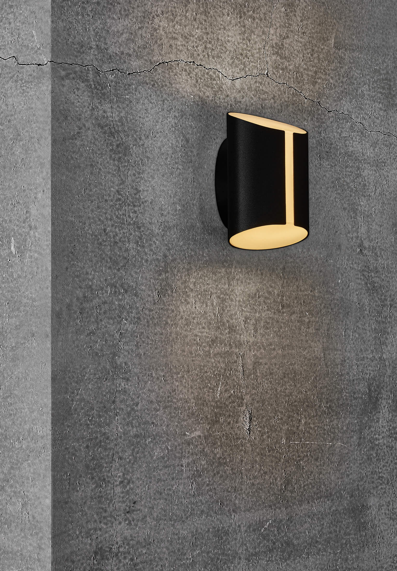 Schwarze Wandleuchte. Schräge Öffnung, die Licht aussendet. Auf einer strukturierten grauen Wand.