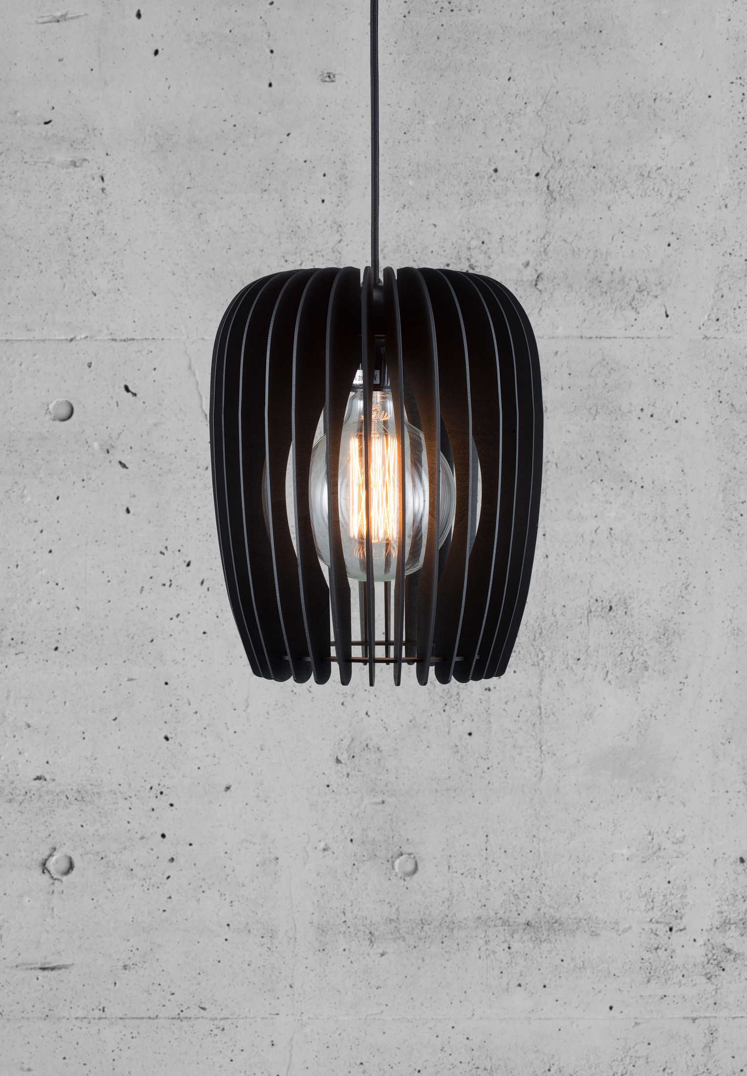 Eine schwarze Pendelleuchte mit einer sichtbaren Glühbirne hängt vor einer grauen Betonwand.