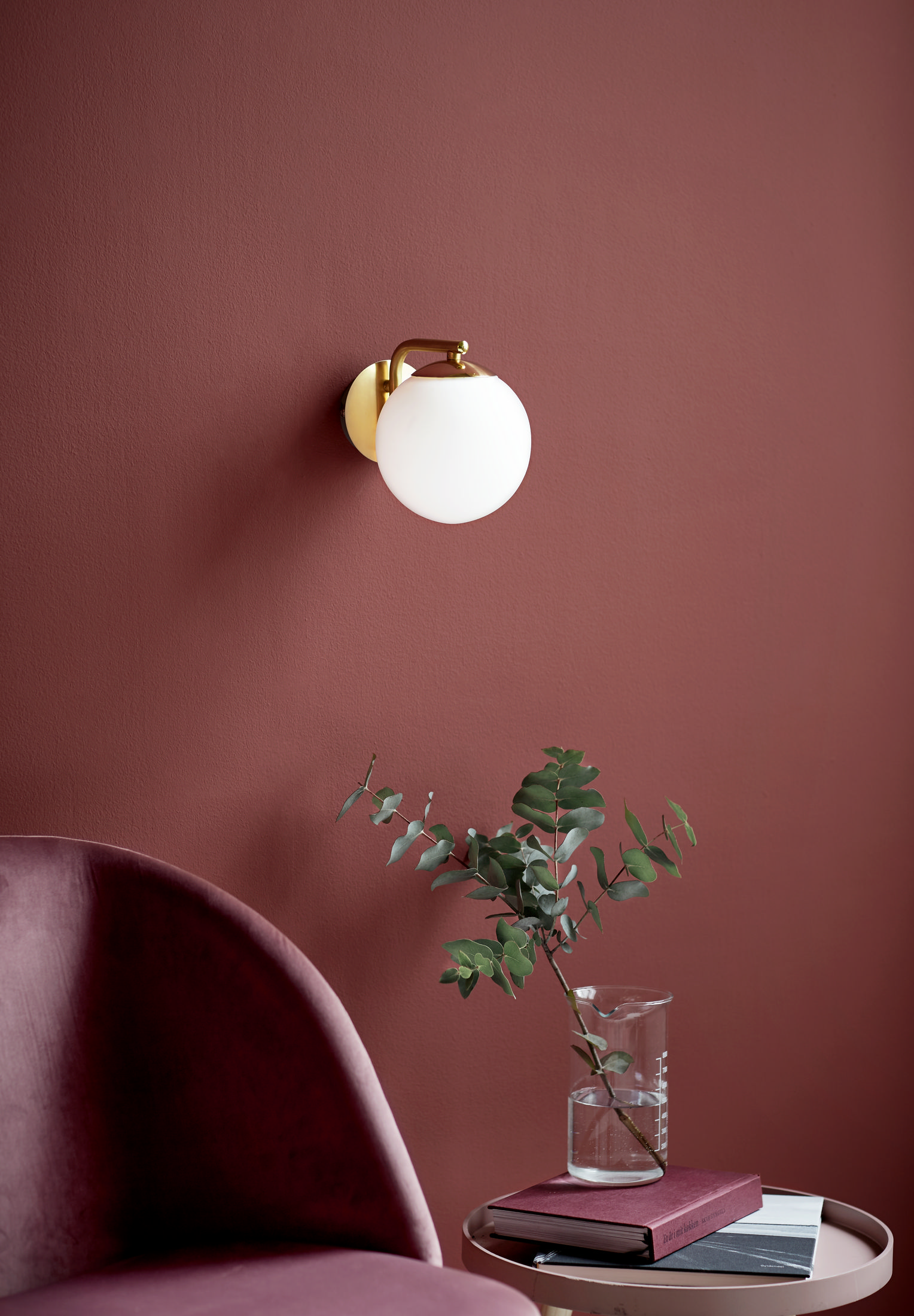 Eine Wandleuchte mit weißem Globus, montiert auf einer goldenen Halterung an einer roten Wand, mit einer Vase.