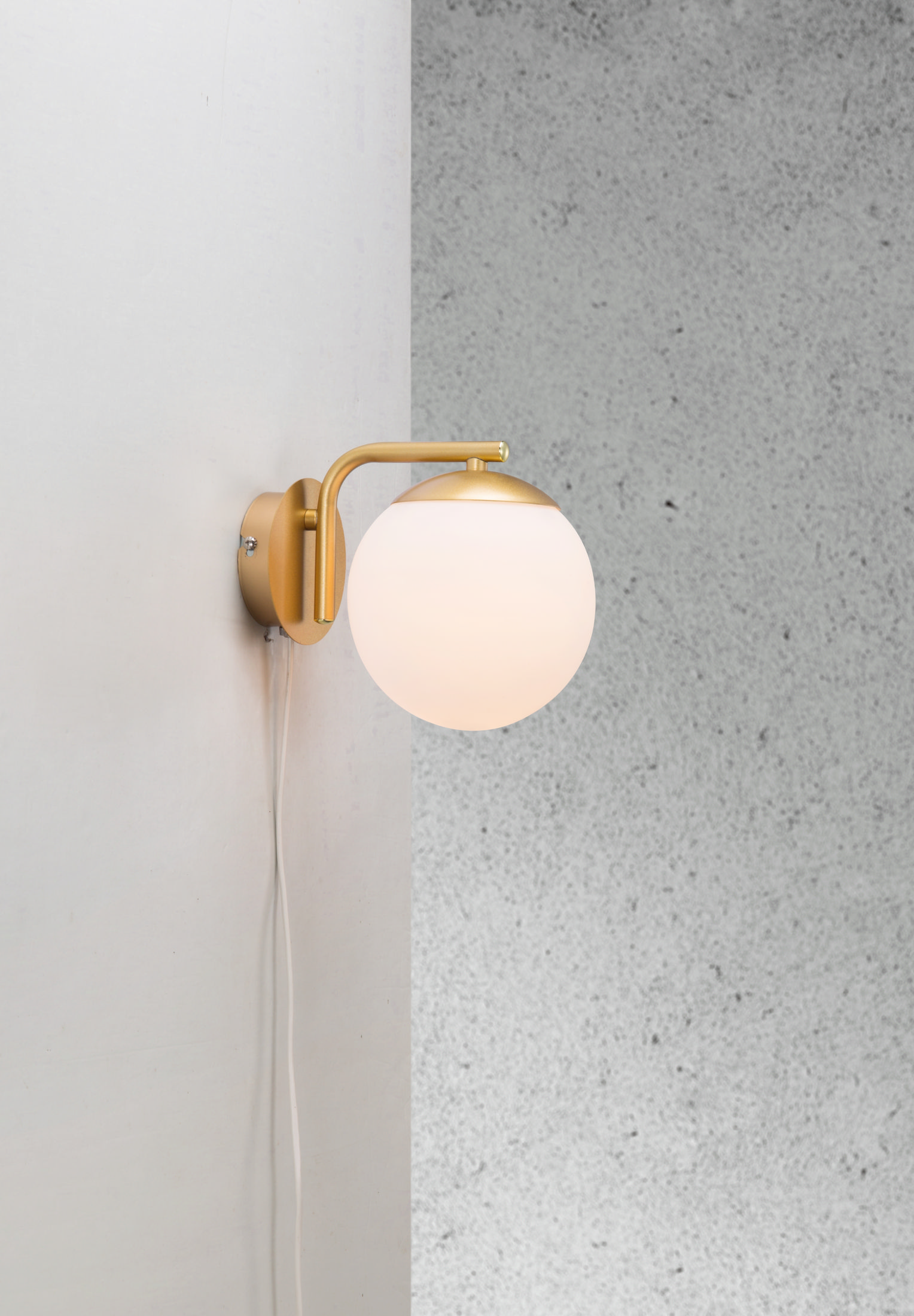 Goldene Wandleuchte mit weißem Kugelschirm an einer grau-weißen Wand.