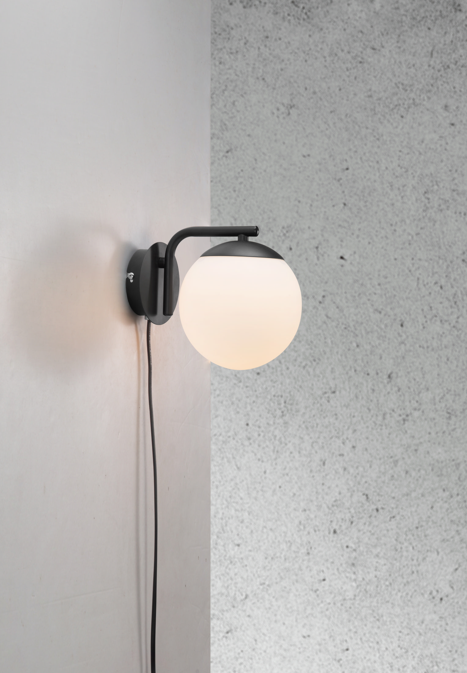 Eine schwarze, an der Wand befestigte Leuchte mit einer weißen Kugel. Die Leuchte befindet sich an einer strukturierten Wand.