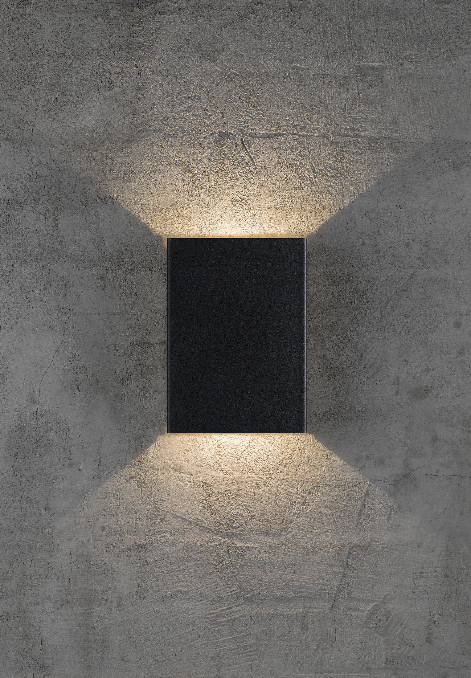 Schwarze rechteckige Wandleuchte an einer grauen Wand. Licht scheint nach oben und unten, erzeugt einen Schein.