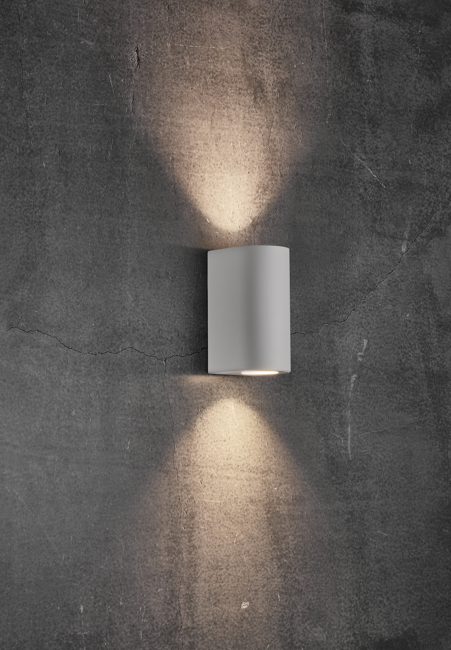 Eine graue Wandleuchte mit Lichtstrahlen, die nach oben und unten gerichtet sind. Der Hintergrund ist eine graue Wand.