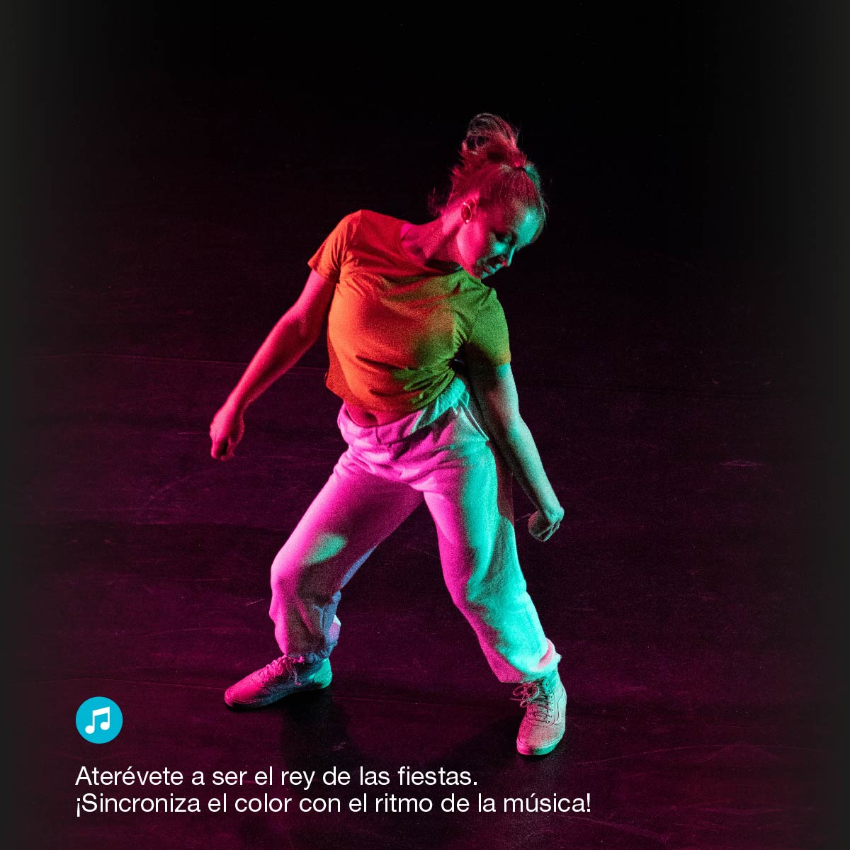 Una mujer bailando en una habitación con una configuración de iluminación colorida, vistiendo ropa naranja y blanca.