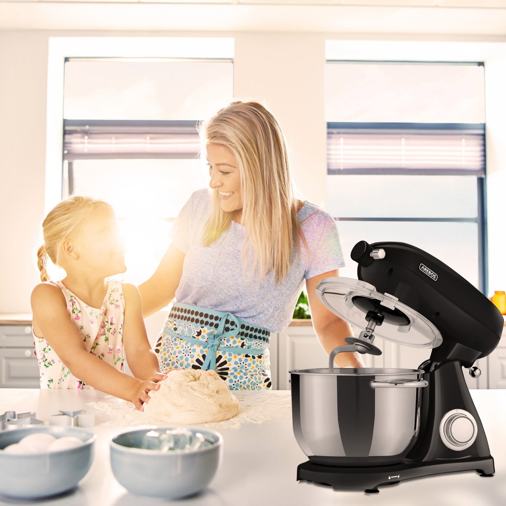 Eine Frau und ein Kind backen in einer Küche. Ein schwarzer Küchenmixer und Schüsseln sind im Vordergrund.