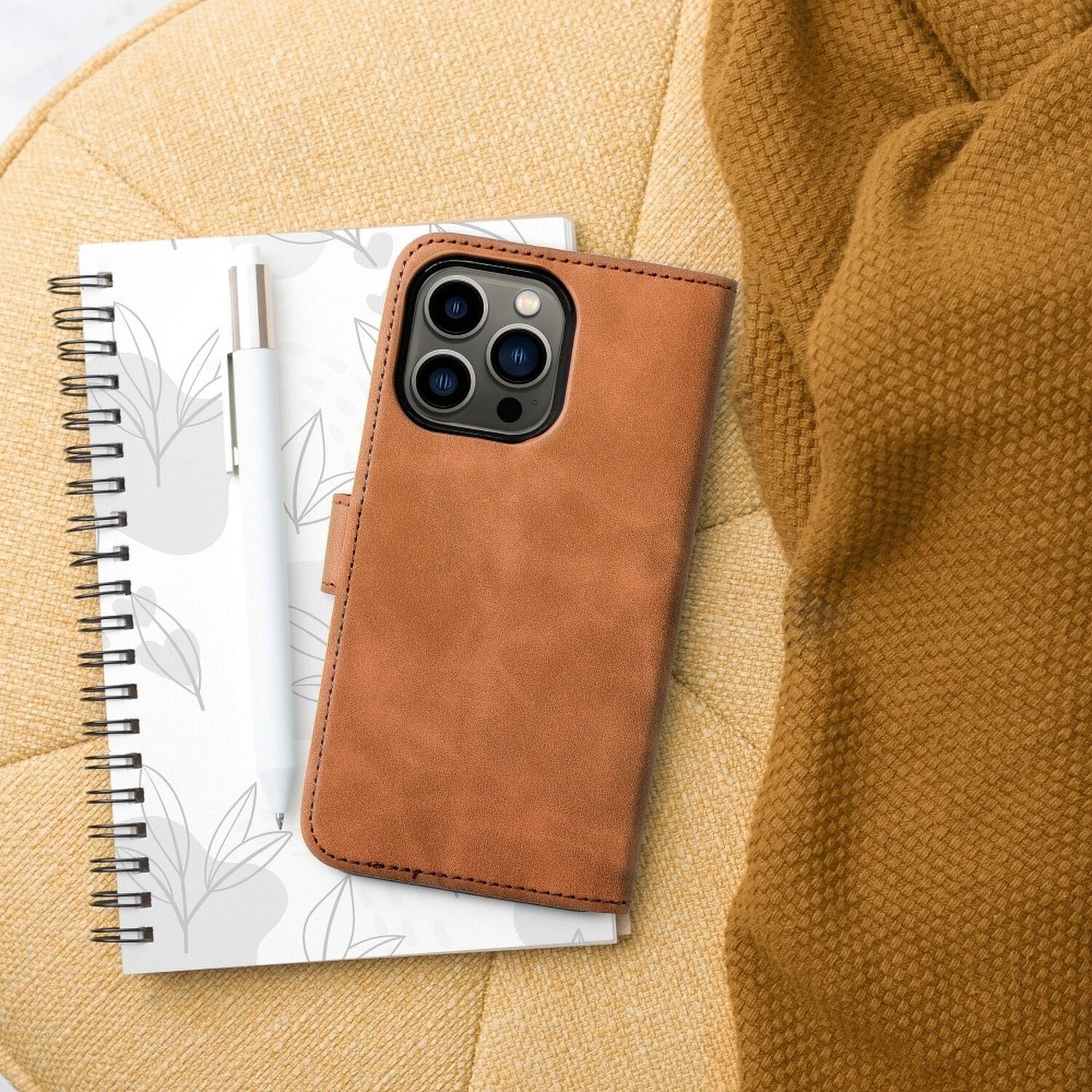 Una custodia per telefono, un quaderno e una penna sono su una sedia gialla accanto a una coperta marrone.