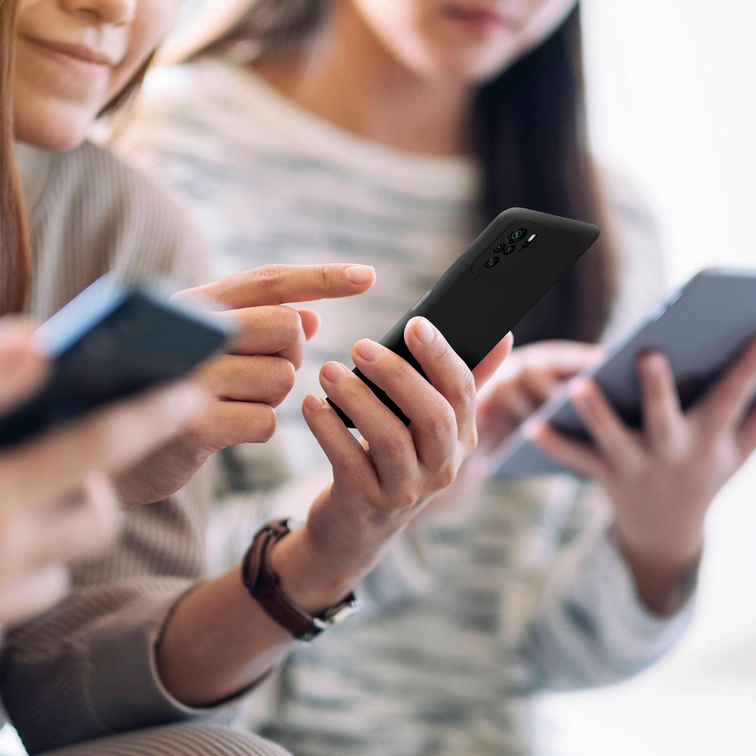 Drei Personen halten und benutzen Smartphones. Ein schwarzes Smartphone wird von einer Frau gehalten.