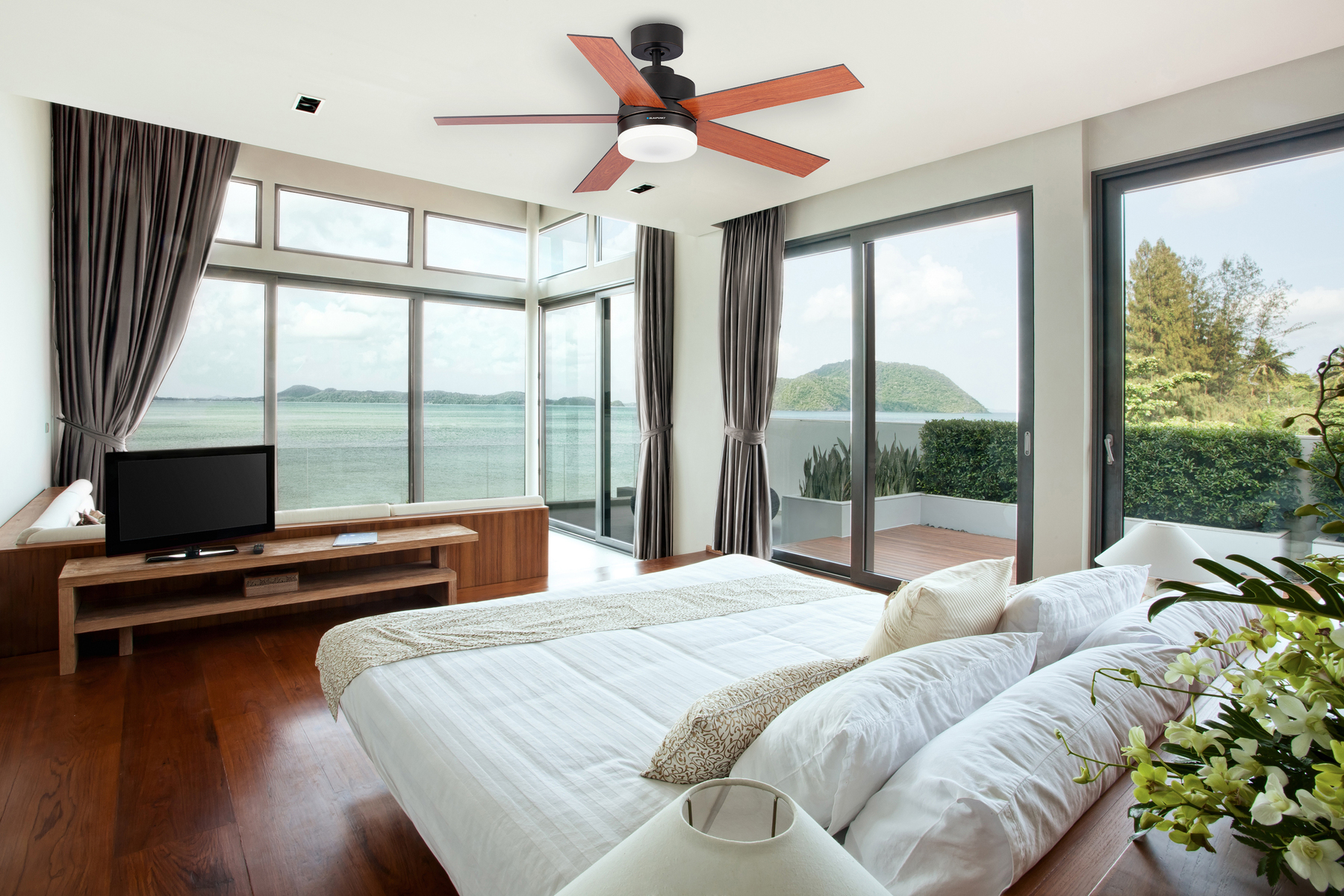 Camera da letto con ventilatore a soffitto, grandi finestre con vista sulla baia. Letto e tende in primo piano.