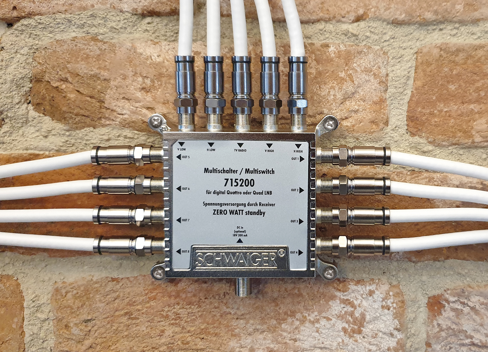 Eine Metallbox mit Anschlüssen. Kabel sind eingesteckt. Es ist vor einer Ziegelmauer.