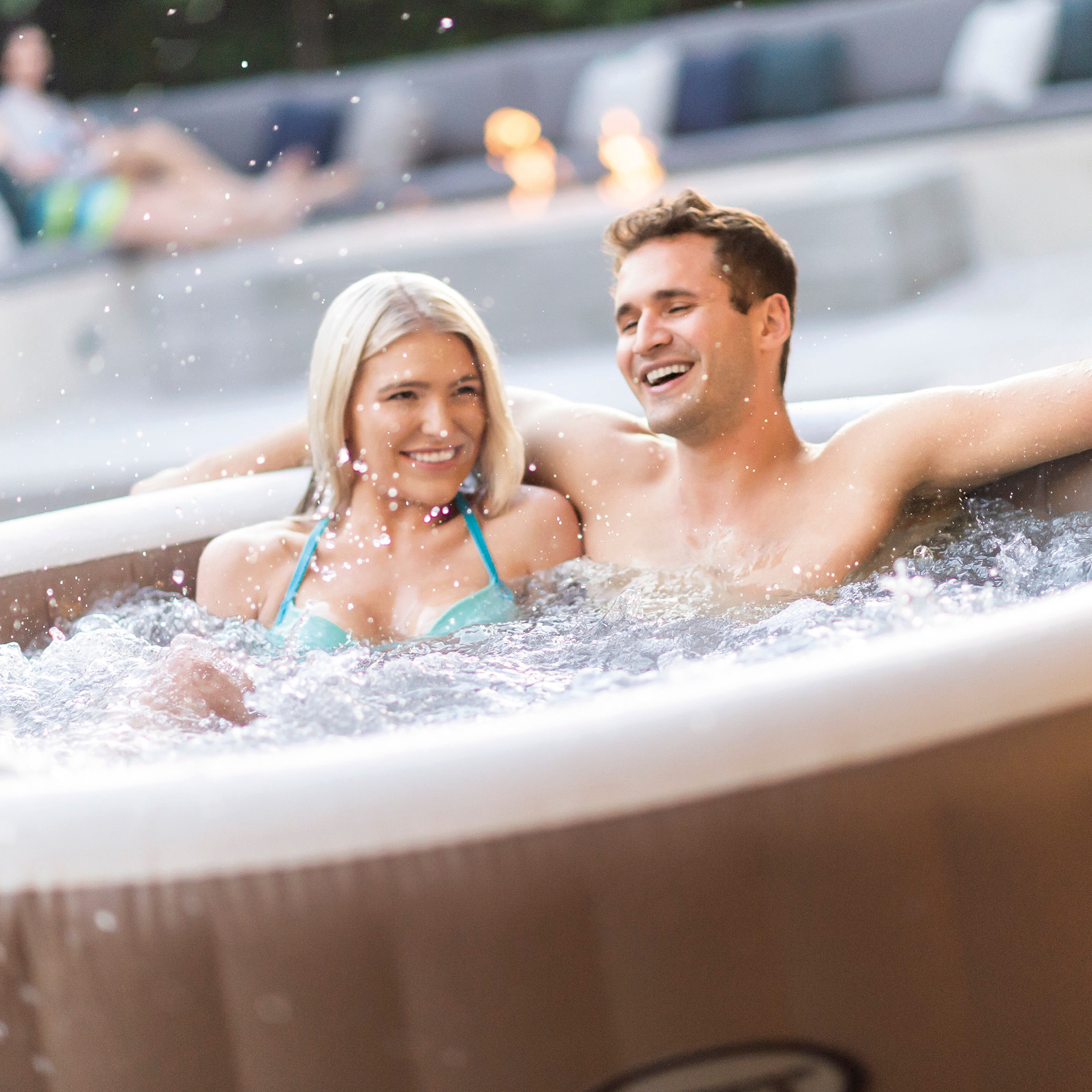Paar im Whirlpool, lächelnd, mit spritzendem Wasser um sie herum.
