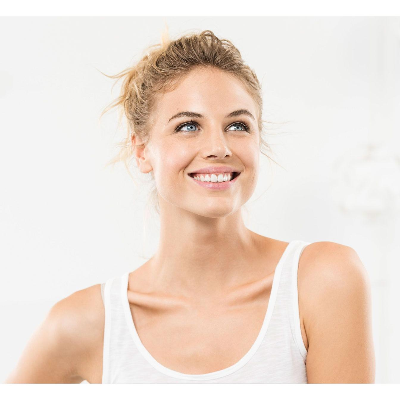 Een vrouw met blond haar glimlacht. Ze draagt een witte tanktop tegen een witte achtergrond.