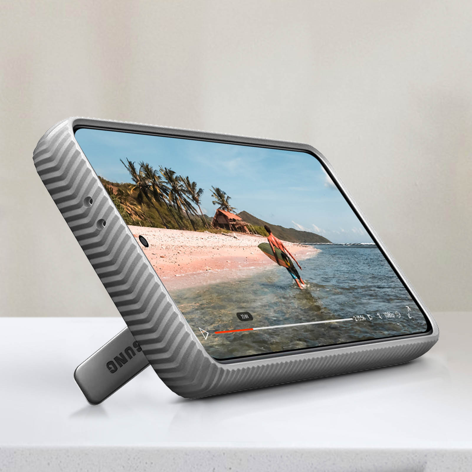 Ein Telefon in einer grauen Hülle, hochgestellt, zeigt eine Strandszene mit einem Surfer.