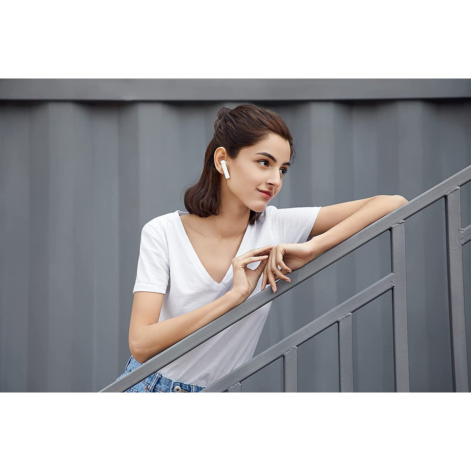 Kobieta w białych słuchawkach, patrząca w prawo, biały t-shirt, dżinsy.