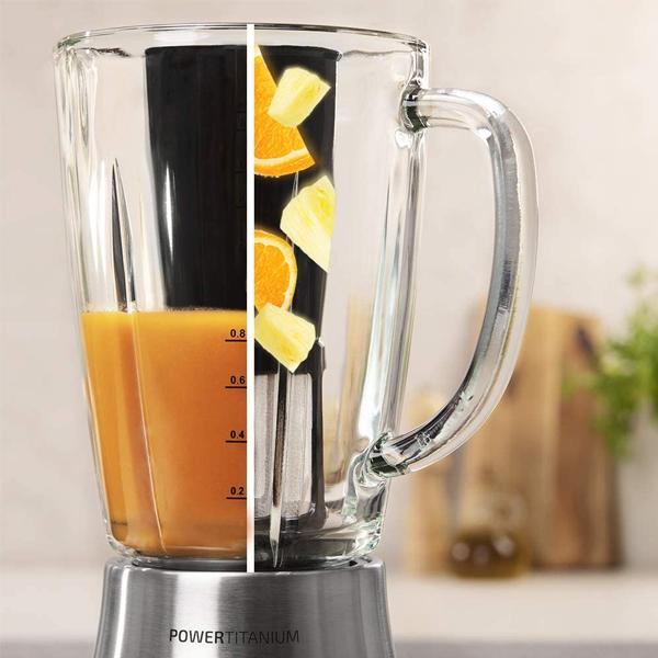 Licuadora con recipiente de vidrio. Jugo de naranja visible. Rodajas de naranja y piña. Base plateada.