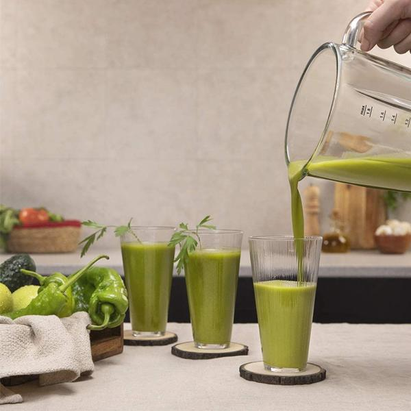 Jugo verde vertiéndose en vasos sobre mesa de madera con ingredientes.