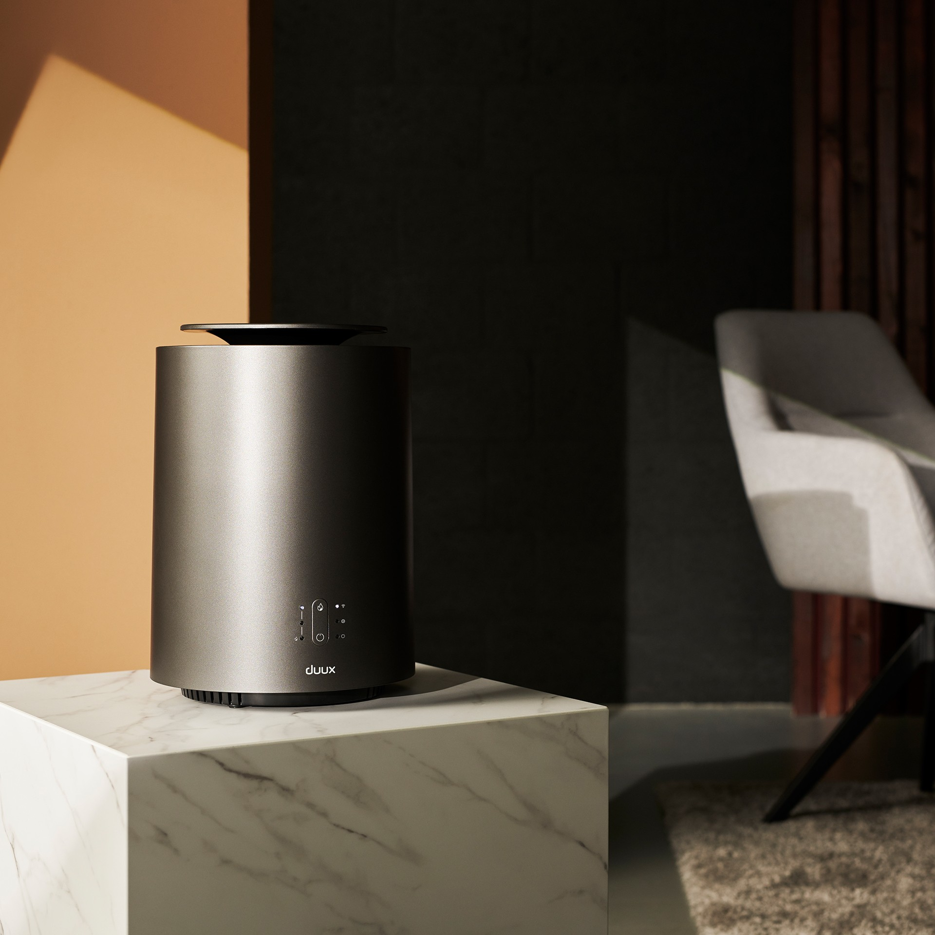 Ciemnoszary cylindryczny oczyszczacz powietrza na marmurowej powierzchni. Krzesło i ciemna ściana w tle.