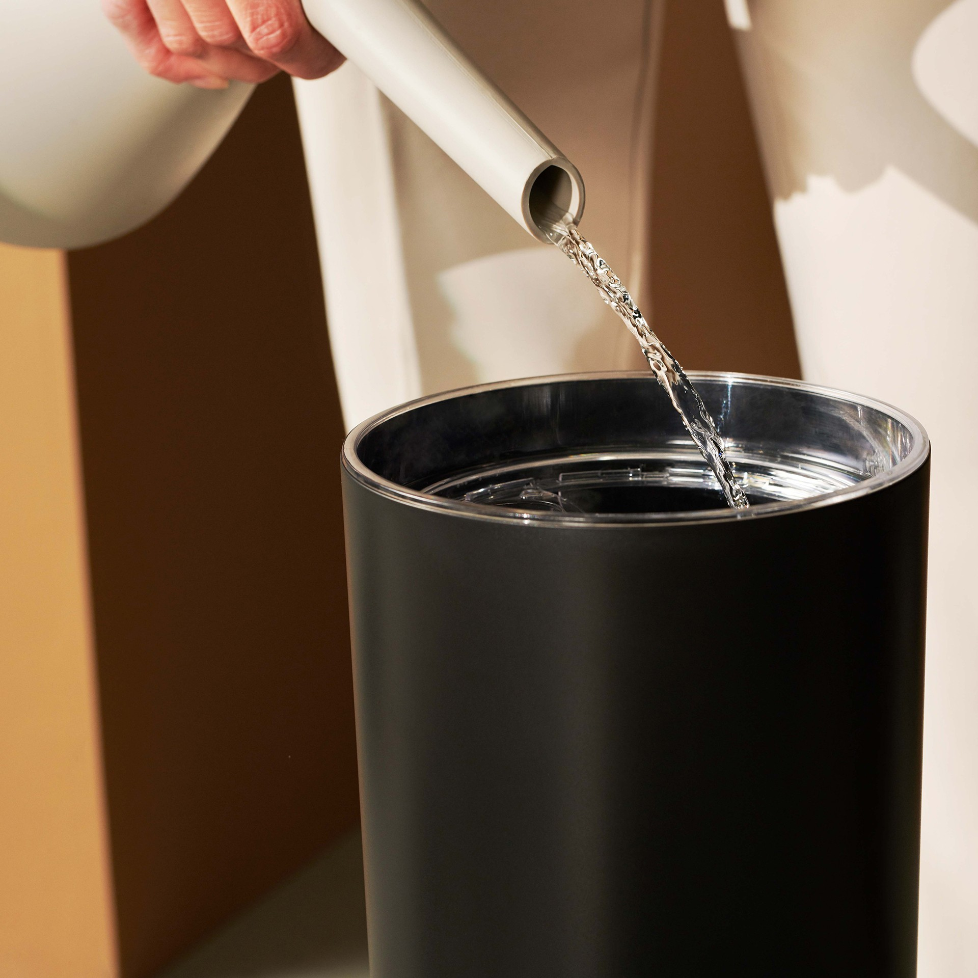 Woda wlewana z białej wylewki do czarnego cylindrycznego pojemnika.