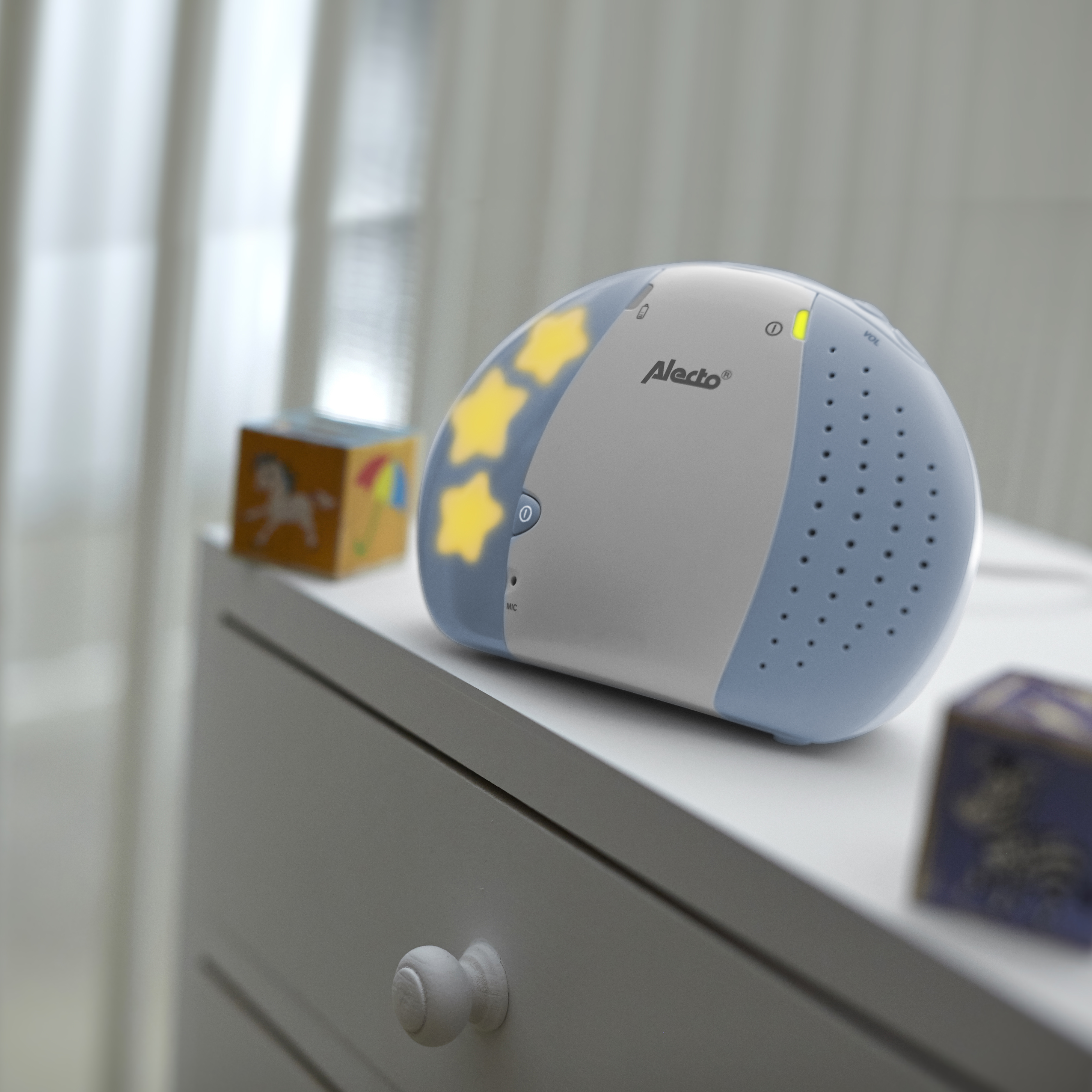 Máquina de sonido para dormir bebés con luces de estrellas y un juguete en una cómoda blanca.